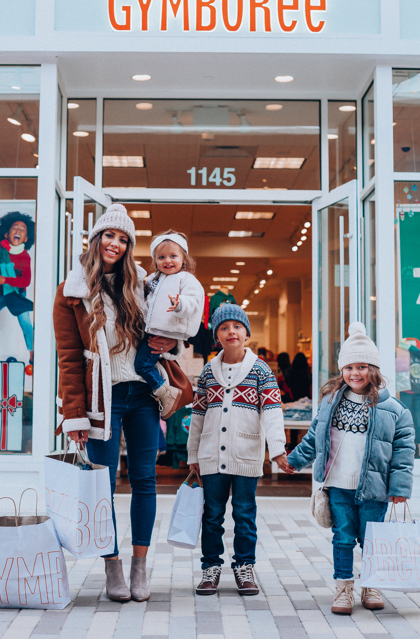 Gymboree Holiday Collection featured by top San Francisco fashion blog, The Girl in the Yellow Dress: image of a mom wearing a Abercrombie & Fitch mock neck sweater, high waist ankle jeans, Mark Fisher Chelsea boots, a pom pom beanie and a leather shoulder bag. A toddler wearing a Gymboree headband, sherpa jacket, sweater, jeggings and metallic moon boots. A boy wearing a Gymboree beanie, sweater, jeans and leather high tops. A girl wearing a Gymboree beanie, coat, sweater, jeans and boots