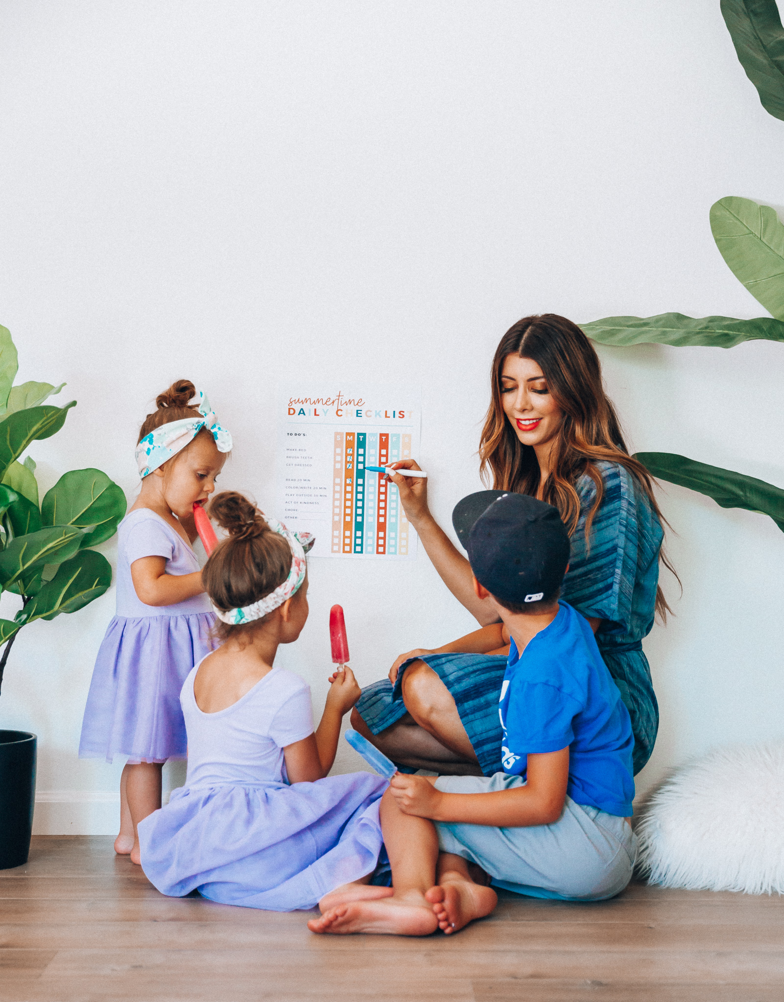 Summer Daily Checklist for Kids by popular San Francisco mom blog, The Girl in the Yellow Dress: image of woman sitting with two young girls and a young boy eating popsicles in front of a daily checklist chart.  Mom is wearing a blue stripe dress, girls are wearing Old Navy Fit & Flare Tutu Dress for Toddler Girls, and the boy is wearing adidas Originals Baby Boys Originals Trefoil Tee, Old Navy Built-In Flex Twill Jogger Shorts for Boys, and ON-FIELD COLLECTION Kids/Youth Yankees 59Fifty Fitted Navy Hat Cap 17GM.