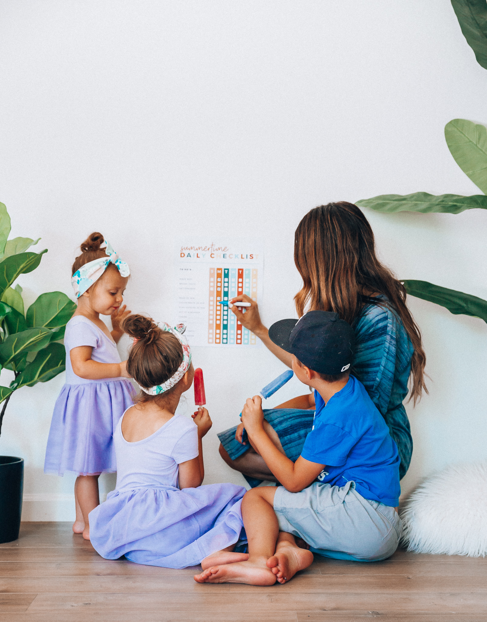 Summer Daily Checklist for Kids by popular San Francisco mom blog, The Girl in the Yellow Dress: image of woman sitting with two young girls and a young boy eating popsicles in front of a daily checklist chart.  Mom is wearing a blue stripe dress, girls are wearing Old Navy Fit & Flare Tutu Dress for Toddler Girls, and the boy is wearing adidas Originals Baby Boys Originals Trefoil Tee, Old Navy Built-In Flex Twill Jogger Shorts for Boys, and ON-FIELD COLLECTION Kids/Youth Yankees 59Fifty Fitted Navy Hat Cap 17GM.