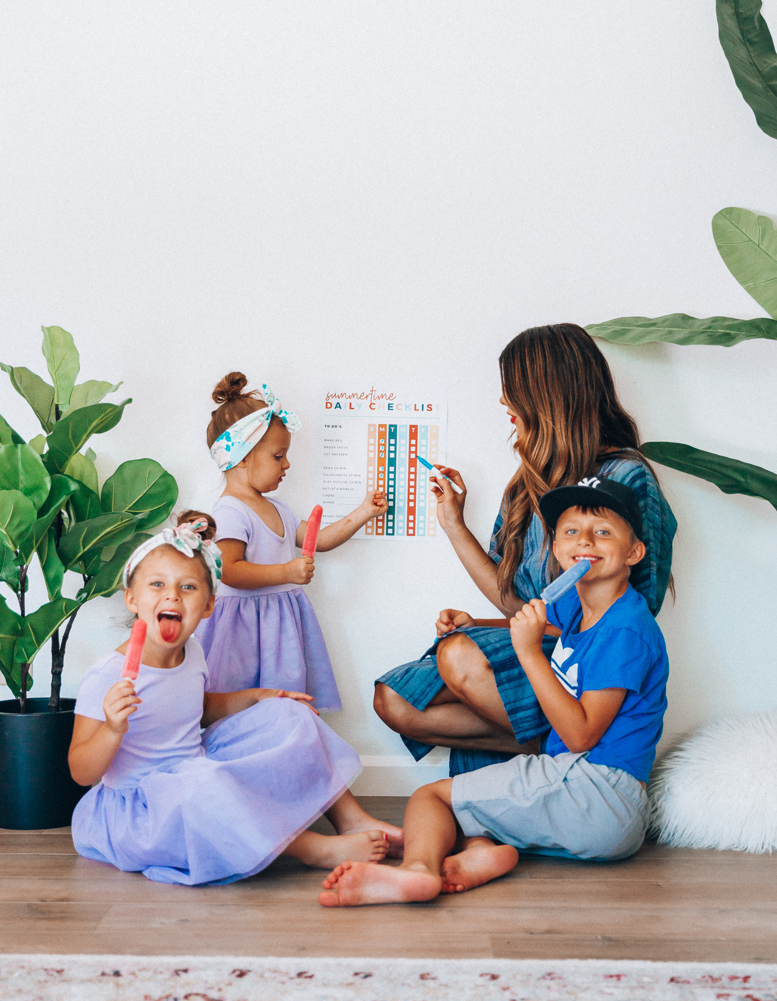 Summer Daily Checklist for Kids by popular San Francisco mom blog, The Girl in the Yellow Dress: image of woman sitting with two young girls and a young boy eating popsicles in front of a daily checklist chart.  Mom is wearing a blue stripe dress, girls are wearing Old Navy Fit & Flare Tutu Dress for Toddler Girls, and the boy is wearing adidas Originals Baby Boys Originals Trefoil Tee, Old Navy Built-In Flex Twill Jogger Shorts for Boys, and ON-FIELD COLLECTION Kids/Youth Yankees 59Fifty Fitted Navy Hat Cap 17GM.