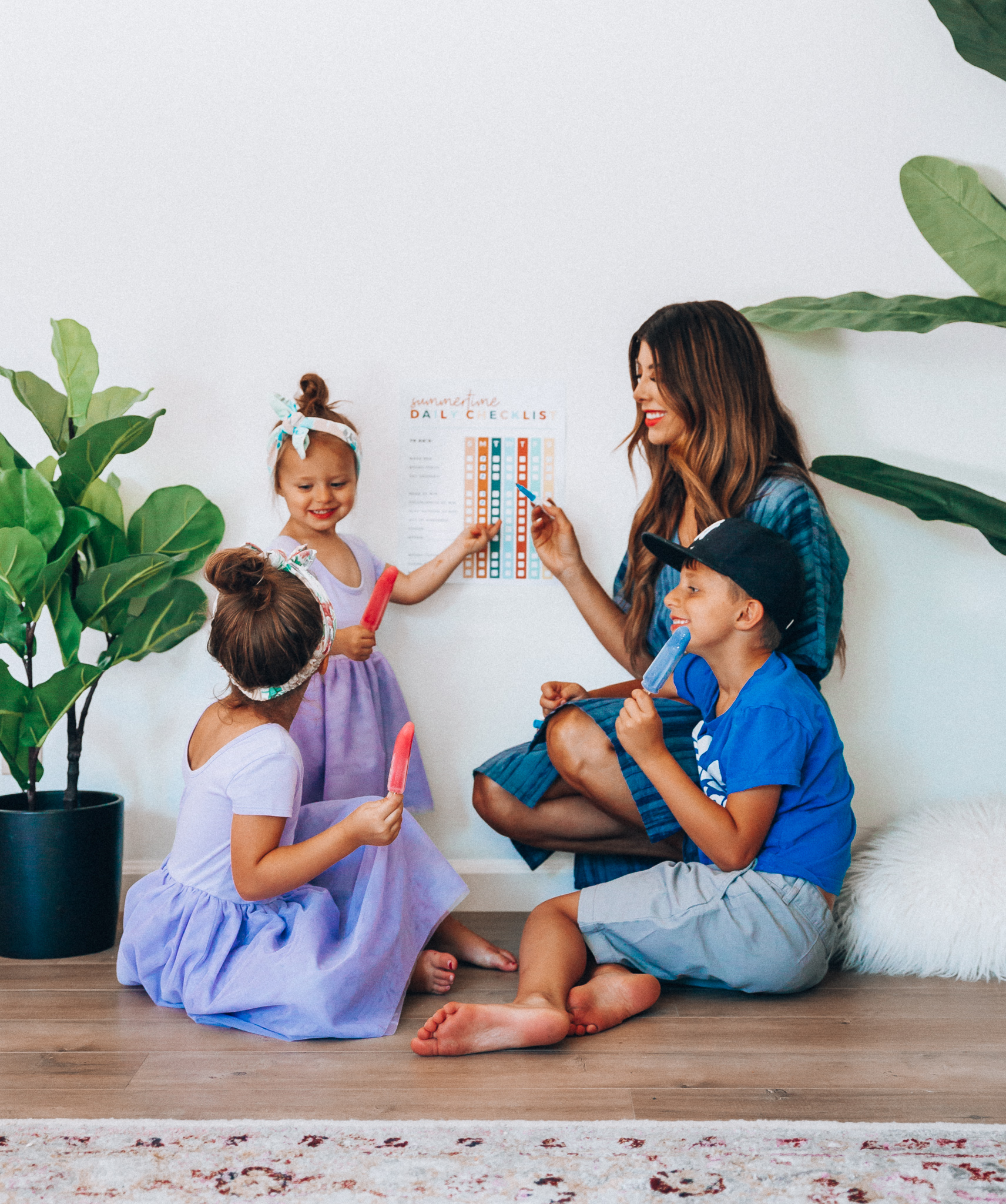 Summer Daily Checklist for Kids by popular San Francisco mom blog, The Girl in the Yellow Dress: image of woman sitting with two young girls and a young boy eating popsicles in front of a daily checklist chart.  Mom is wearing a blue stripe dress, girls are wearing Old Navy Fit & Flare Tutu Dress for Toddler Girls, and the boy is wearing adidas Originals Baby Boys Originals Trefoil Tee, Old Navy Built-In Flex Twill Jogger Shorts for Boys, and ON-FIELD COLLECTION Kids/Youth Yankees 59Fifty Fitted Navy Hat Cap 17GM.