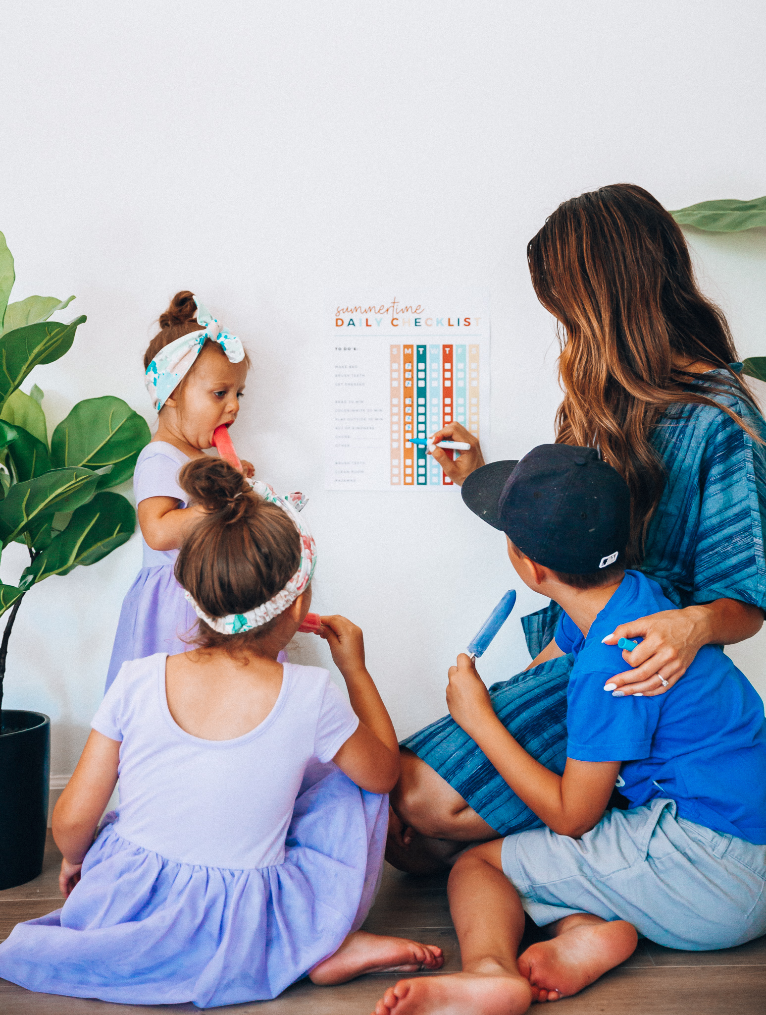 Summer Daily Checklist for Kids by popular San Francisco mom blog, The Girl in the Yellow Dress: image of woman standing with two young girls and a young boy eating popsicles next to a daily checklist chart.  Mom is wearing a blue stripe dress, girls are wearing Old Navy Fit & Flare Tutu Dress for Toddler Girls, and the boy is wearing adidas Originals Baby Boys Originals Trefoil Tee, Old Navy Built-In Flex Twill Jogger Shorts for Boys, and ON-FIELD COLLECTION Kids/Youth Yankees 59Fifty Fitted Navy Hat Cap 17GM.