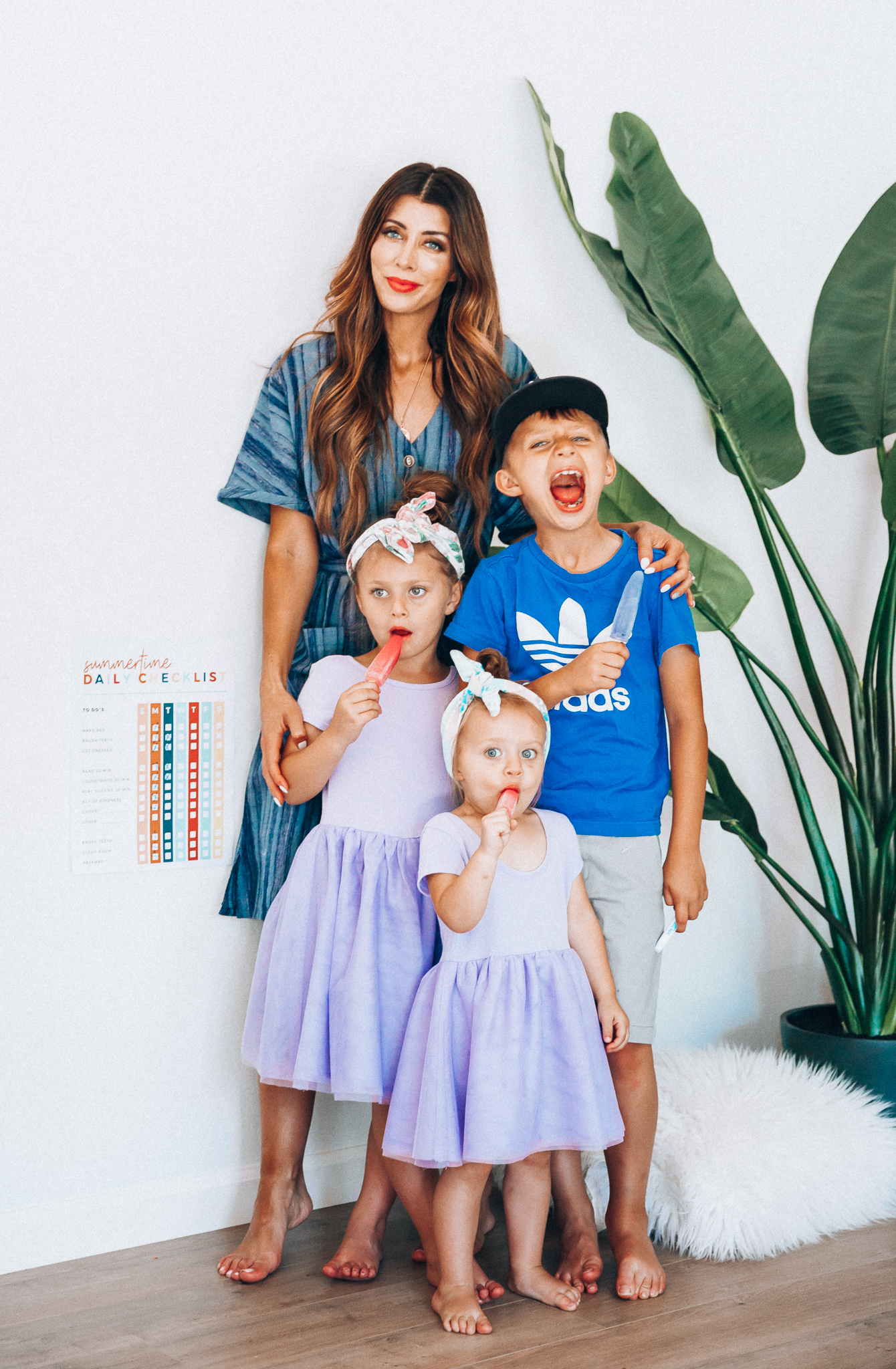 Summer Daily Checklist for Kids by popular San Francisco mom blog, The Girl in the Yellow Dress: image of woman standing with two young girls and a young boy eating popsicles next to a daily checklist chart.  Mom is wearing a blue stripe dress, girls are wearing Old Navy Fit & Flare Tutu Dress for Toddler Girls, and the boy is wearing adidas Originals Baby Boys Originals Trefoil Tee, Old Navy Built-In Flex Twill Jogger Shorts for Boys, and ON-FIELD COLLECTION Kids/Youth Yankees 59Fifty Fitted Navy Hat Cap 17GM.