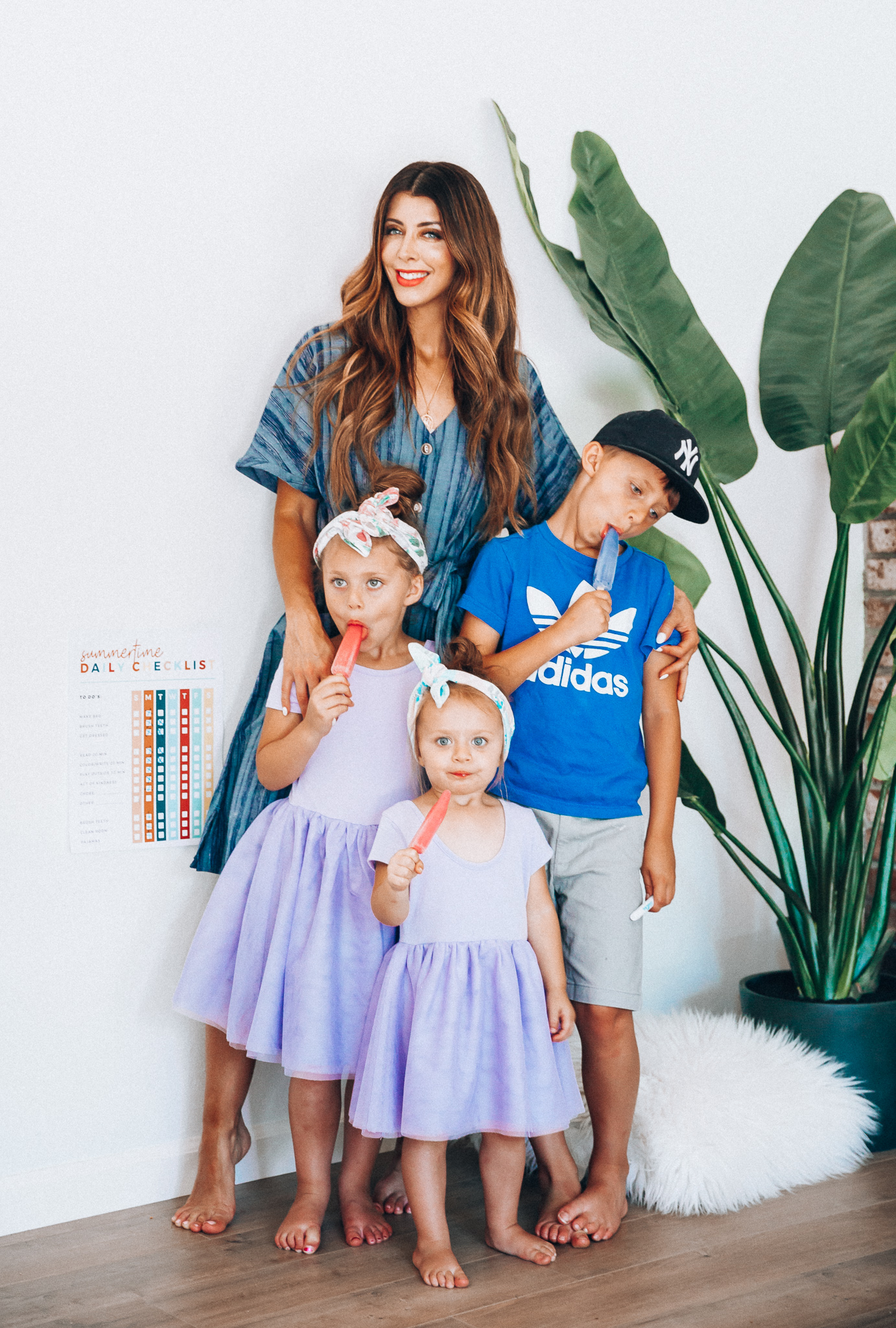 Summer Daily Checklist for Kids by popular San Francisco mom blog, The Girl in the Yellow Dress: image of woman standing with two young girls and a young boy eating popsicles next to a daily checklist chart.  Mom is wearing a blue stripe dress, girls are wearing Old Navy Fit & Flare Tutu Dress for Toddler Girls, and the boy is wearing adidas Originals Baby Boys Originals Trefoil Tee, Old Navy Built-In Flex Twill Jogger Shorts for Boys, and ON-FIELD COLLECTION Kids/Youth Yankees 59Fifty Fitted Navy Hat Cap 17GM.