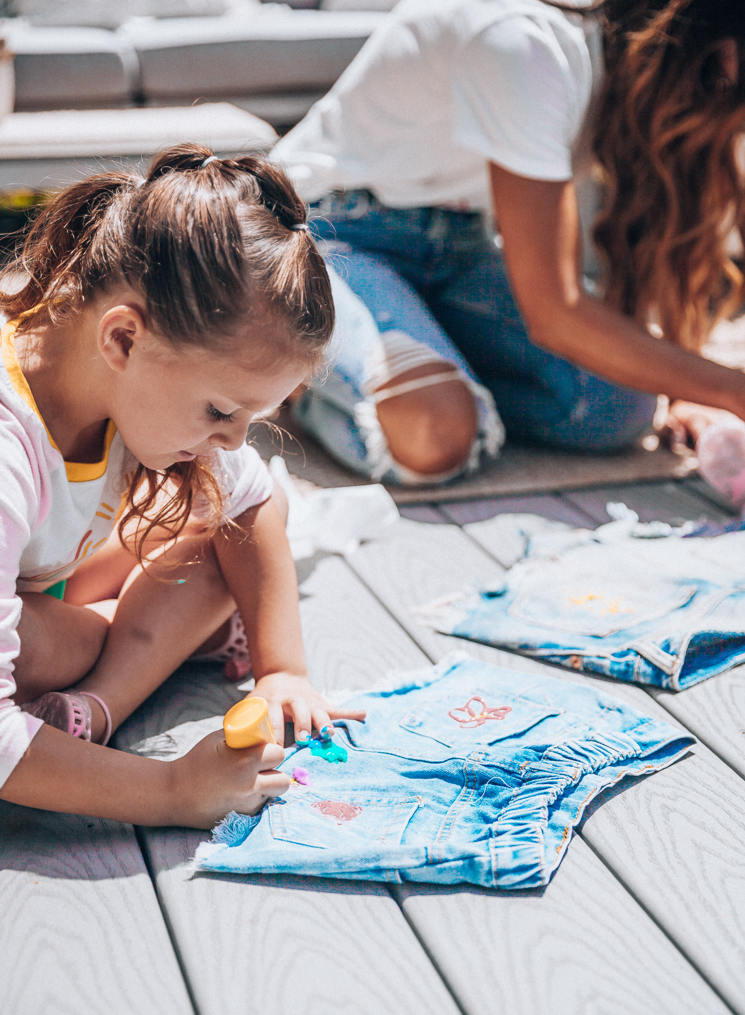 The Girl in the Yellow Dress | Latisha Springer | Fun Summer Activities for Kids by top US mom blog, The Girl in the Yellow Dress: image of mom with young girl sitting on back porch deck decorating cutoff denim shorts with puff paint.