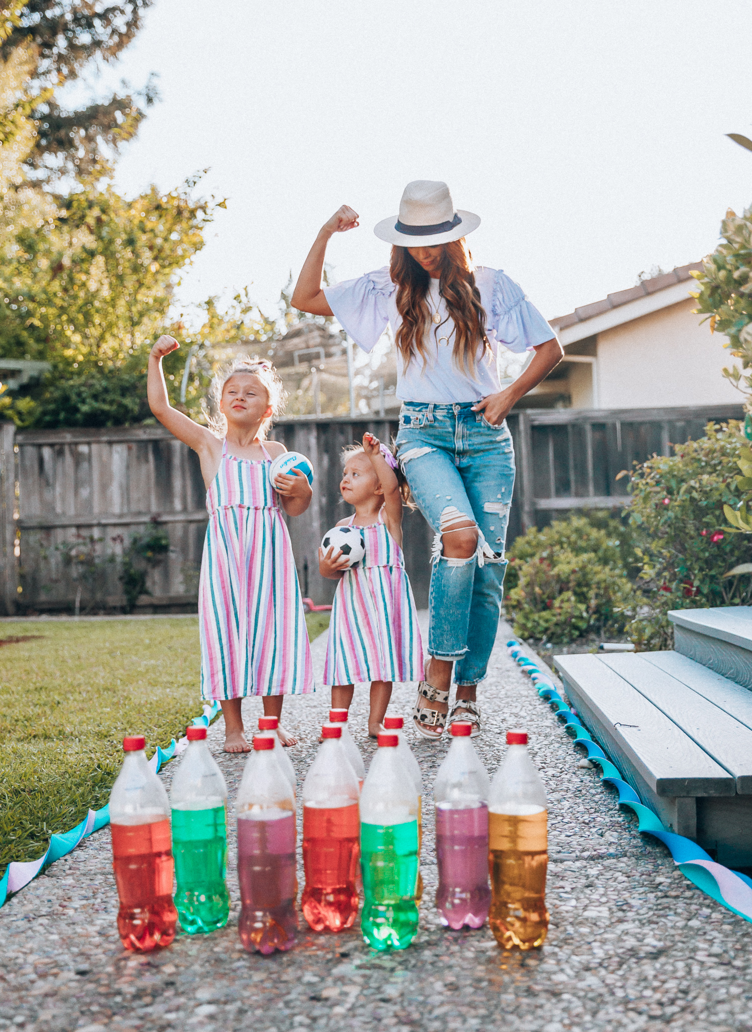 Fun Summer Activities for Kids-Part 2 by popular mom blog The Girl in the Yellow Dress: image of woman and two young girls playing outdoor bowling.  Woman is wearing a Brixton Joanna Straw Hat, Naughty Monkey Women's Hey Pony Sandal, Abercrombie and Fitch Boyfriend jeans, and a Nordstrom ruffle sleeve top.  Girls are wearing an Oldnavy Striped Ruffle-Trim Halter Midi Dress. 