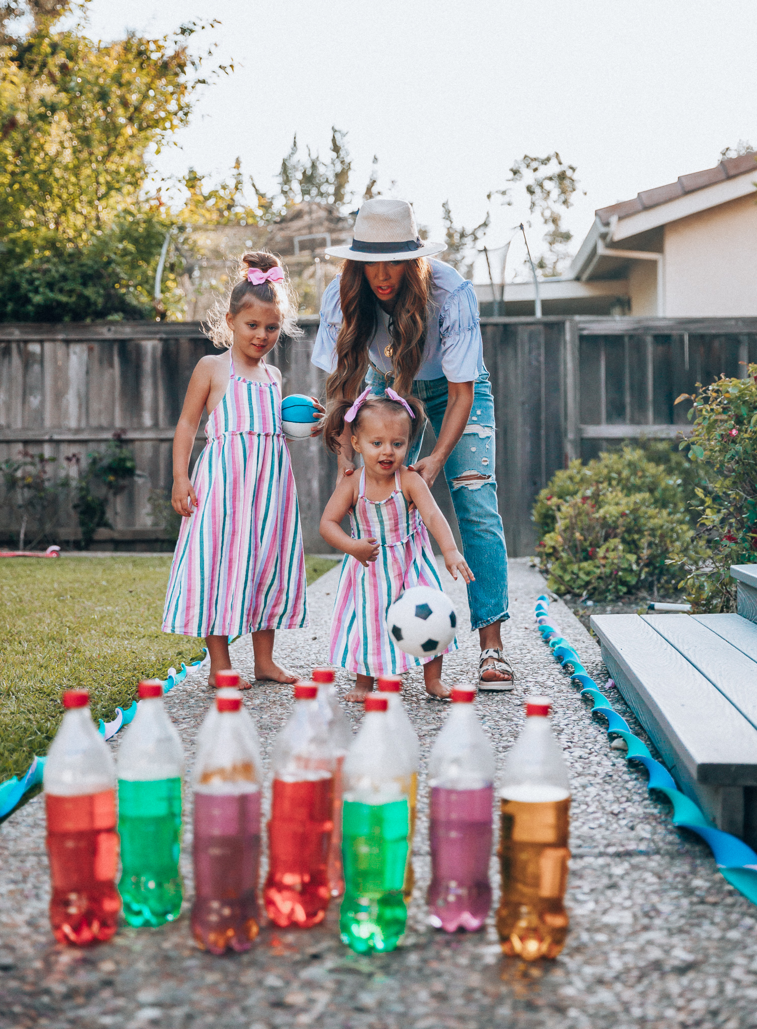 Fun Summer Activities for Kids-Part 2 by popular mom blog The Girl in the Yellow Dress: image of woman and two young girls playing outdoor bowling.  Woman is wearing a Brixton Joanna Straw Hat, Naughty Monkey Women's Hey Pony Sandal, Abercrombie and Fitch Boyfriend jeans, and a Nordstrom ruffle sleeve top.  Girls are wearing an Oldnavy Striped Ruffle-Trim Halter Midi Dress. 