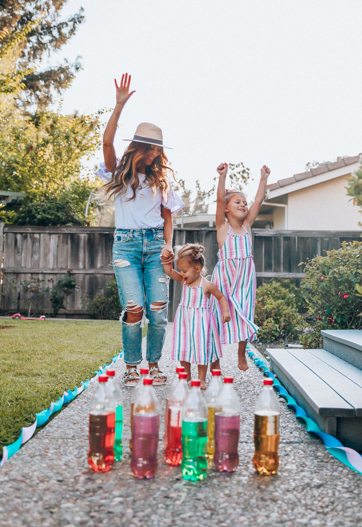 Fun Summer Activities for Kids-Part 2 by popular mom blog The Girl in the Yellow Dress: image of woman and two young girls playing outdoor bowling.  Woman is wearing a Brixton Joanna Straw Hat, Naughty Monkey Women's Hey Pony Sandal, Abercrombie and Fitch Boyfriend jeans, and a Nordstrom ruffle sleeve top.  Girls are wearing an Oldnavy Striped Ruffle-Trim Halter Midi Dress. 