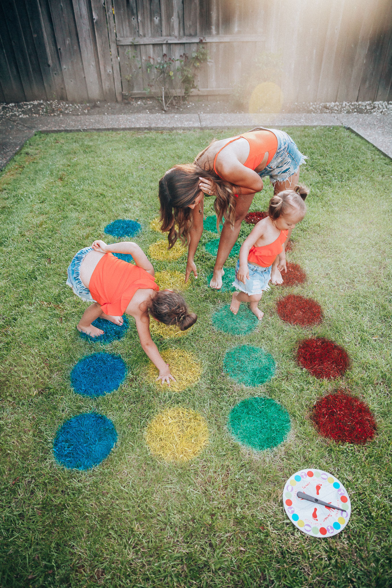 The Girl in the Yellow Dress | Latisha Springer | Fun Summer Activities for Kids by top US mom blog, The Girl in the Yellow Dress: image of mom, young kids, backyard, grass, cutoff shorts, red swimming suit tops, and twister game.