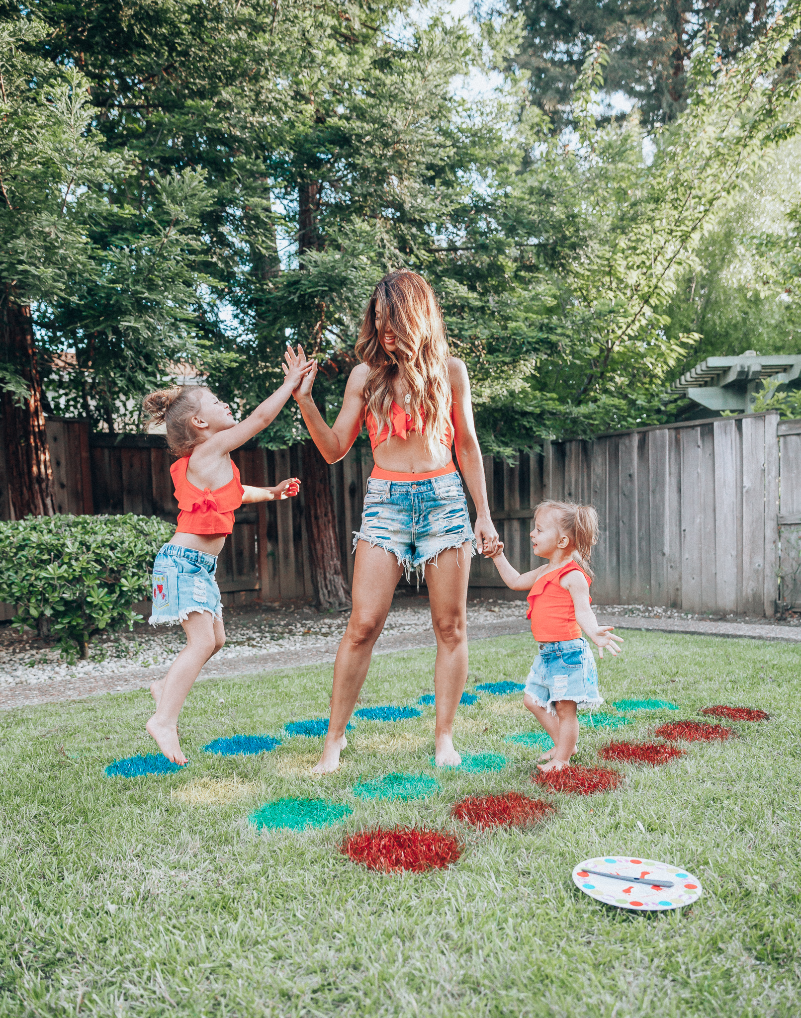 The Girl in the Yellow Dress | Latisha Springer | Fun Summer Activities for Kids by top US mom blog, The Girl in the Yellow Dress: image of mom, young kids, backyard, grass, cutoff shorts, red swimming suit tops, and twister game.