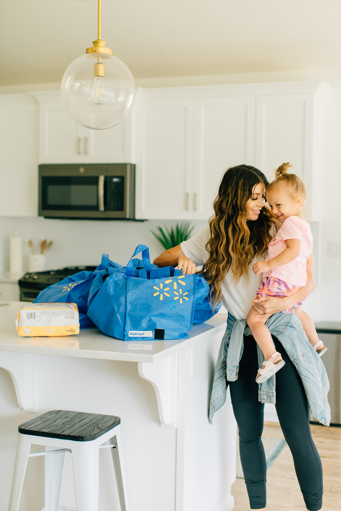 Walmart Grocery Pick Up Review! by popular San Francisco lifestyle blog, The Girl in the Yellow Dress: image of a mom holding her daughter in their kitchen with some re-usable Walmart shopping bags on their kitchen counter.