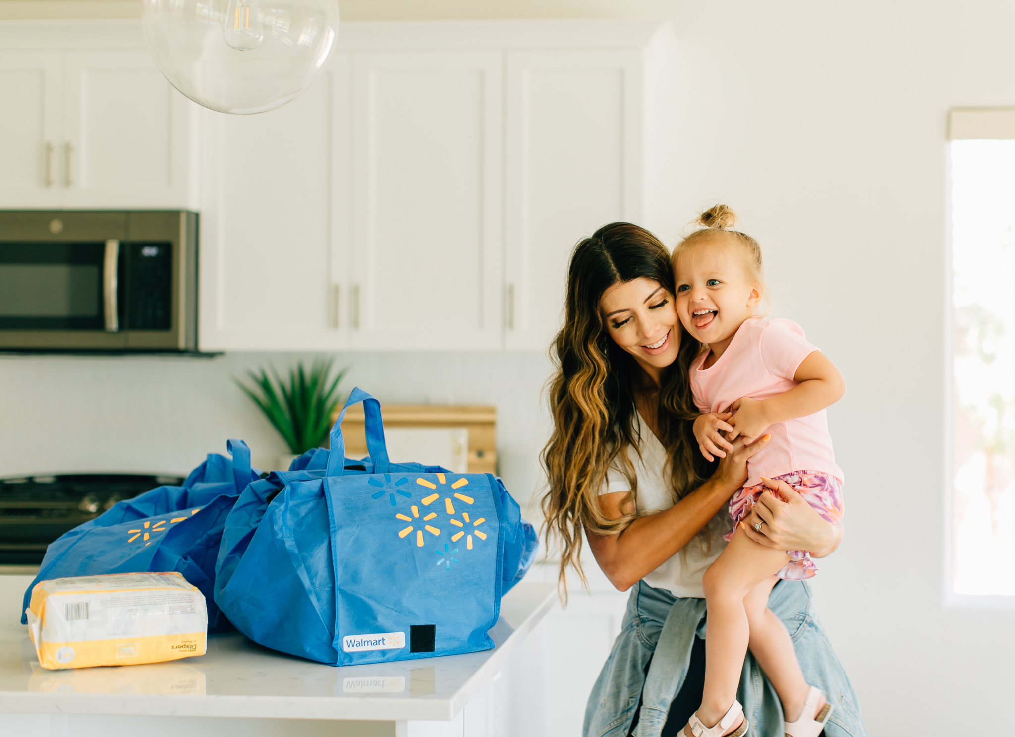 Walmart Grocery Pick Up Review! by popular San Francisco lifestyle blog, The Girl in the Yellow Dress: image of a mom holding her daughter in their kitchen with some re-usable Walmart shopping bags on their kitchen counter.