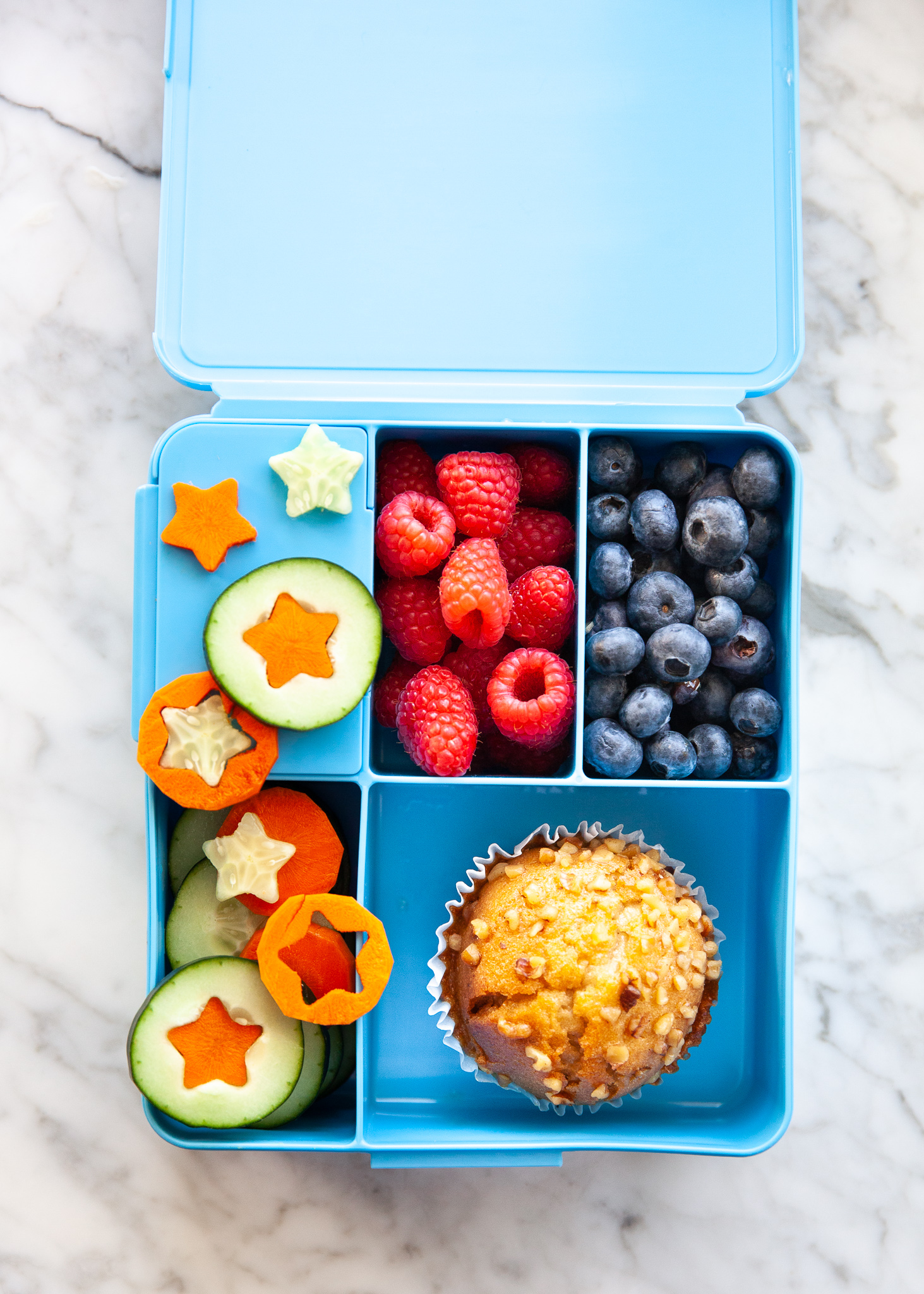 Easy Back to School Lunch Ideas! by popular San Francisco lifestyle blog, The Girl in the Yellow Dress: collage image of Pottery Barn Kids Spencer Bento Box Containers with it's compartments filled with cucumbers and carrots cut into stars by a LENK Vegetable Cutter Shapes Set, blueberries, raspberries, and a muffin.