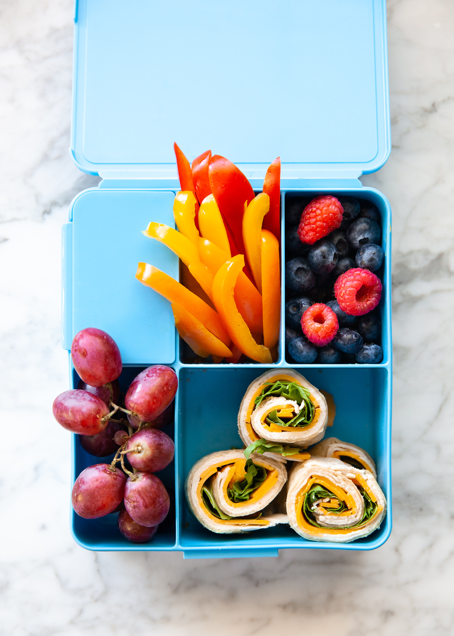 Easy Back to School Lunch Ideas! by popular San Francisco lifestyle blog, The Girl in the Yellow Dress: collage image of Pottery Barn Kids Spencer Bento Box Containers with it's compartments filled with grapes, blueberries and raspberries, turkey rollups, and pepper slices. 