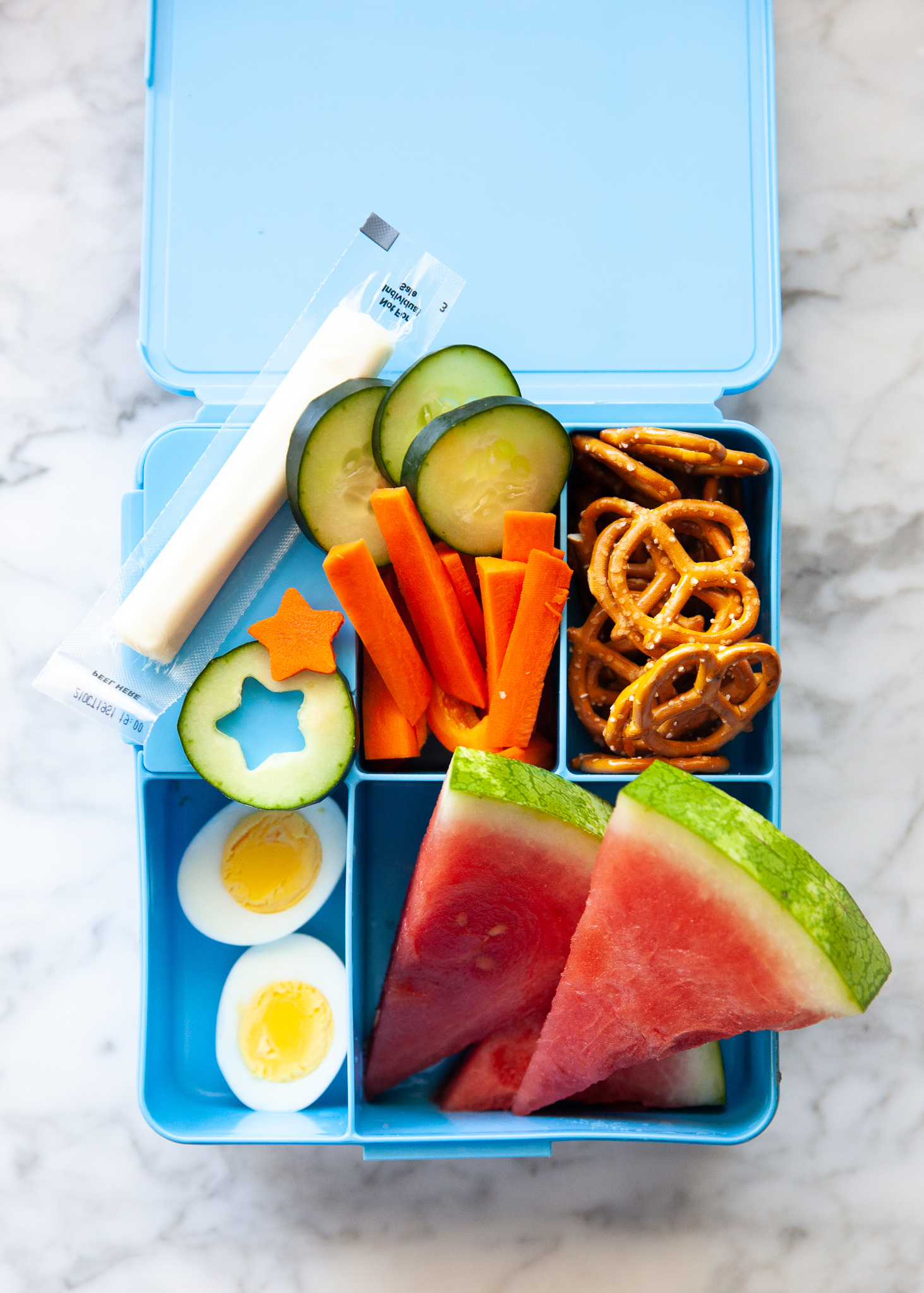 Easy Back to School Lunch Ideas! by popular San Francisco lifestyle blog, The Girl in the Yellow Dress: collage image of Pottery Barn Kids Spencer Bento Box Containers with it's compartments filled with cucumbers and carrots cute into stars by a LENK Vegetable Cutter Shapes Set, pretzels, string cheese, carrot sticks, cucumber slices, watermelon slices, and hard boiled eggs.