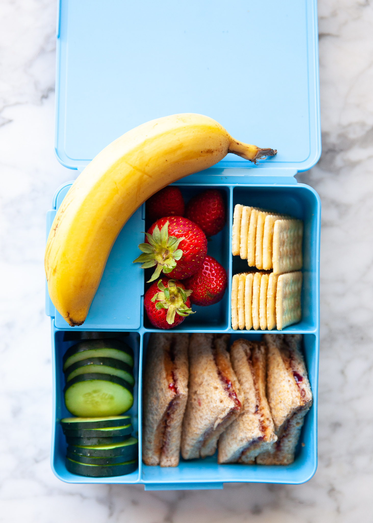 Easy Back to School Lunch Ideas! by popular San Francisco lifestyle blog, The Girl in the Yellow Dress: collage image of Pottery Barn Kids Spencer Bento Box Containers with it's compartments filled with crackers, banana, strawberries, cucumber slices and peanut butter and jelly triangle sandwiches.