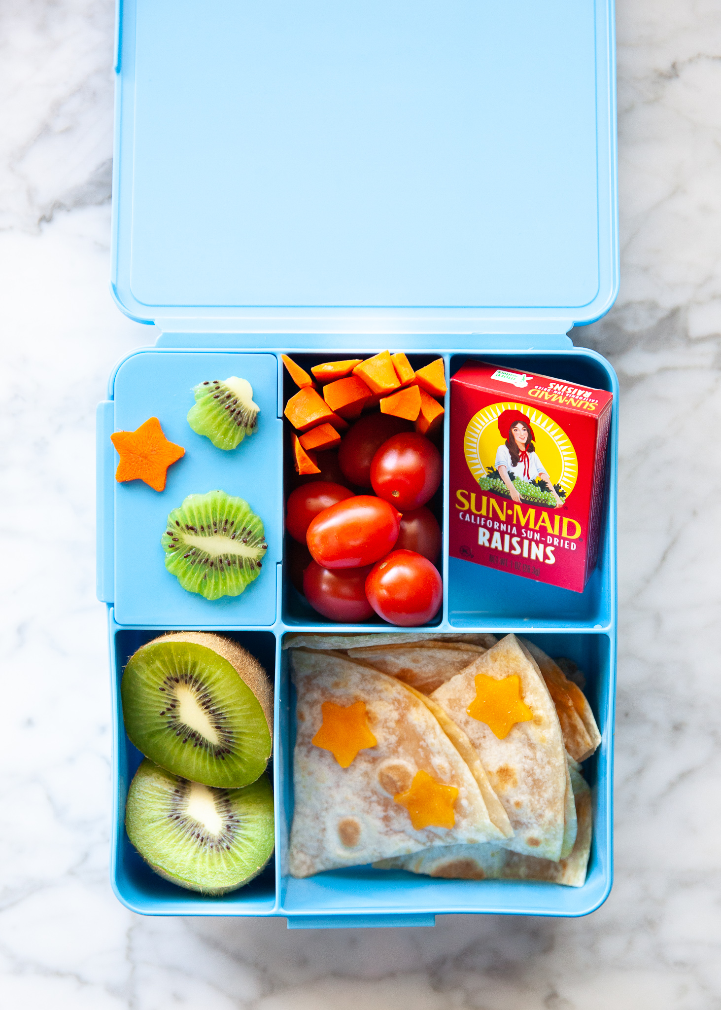 Easy Back to School Lunch Ideas! by popular San Francisco lifestyle blog, The Girl in the Yellow Dress: collage image of Pottery Barn Kids Spencer Bento Box Containers with it's compartments filled with kiwi and carrots cut into stars by a LENK Vegetable Cutter Shapes Set, box of raisins, cherry tomatoes, carrot sticks, kiwi halves, and cheese quesadilla slices.