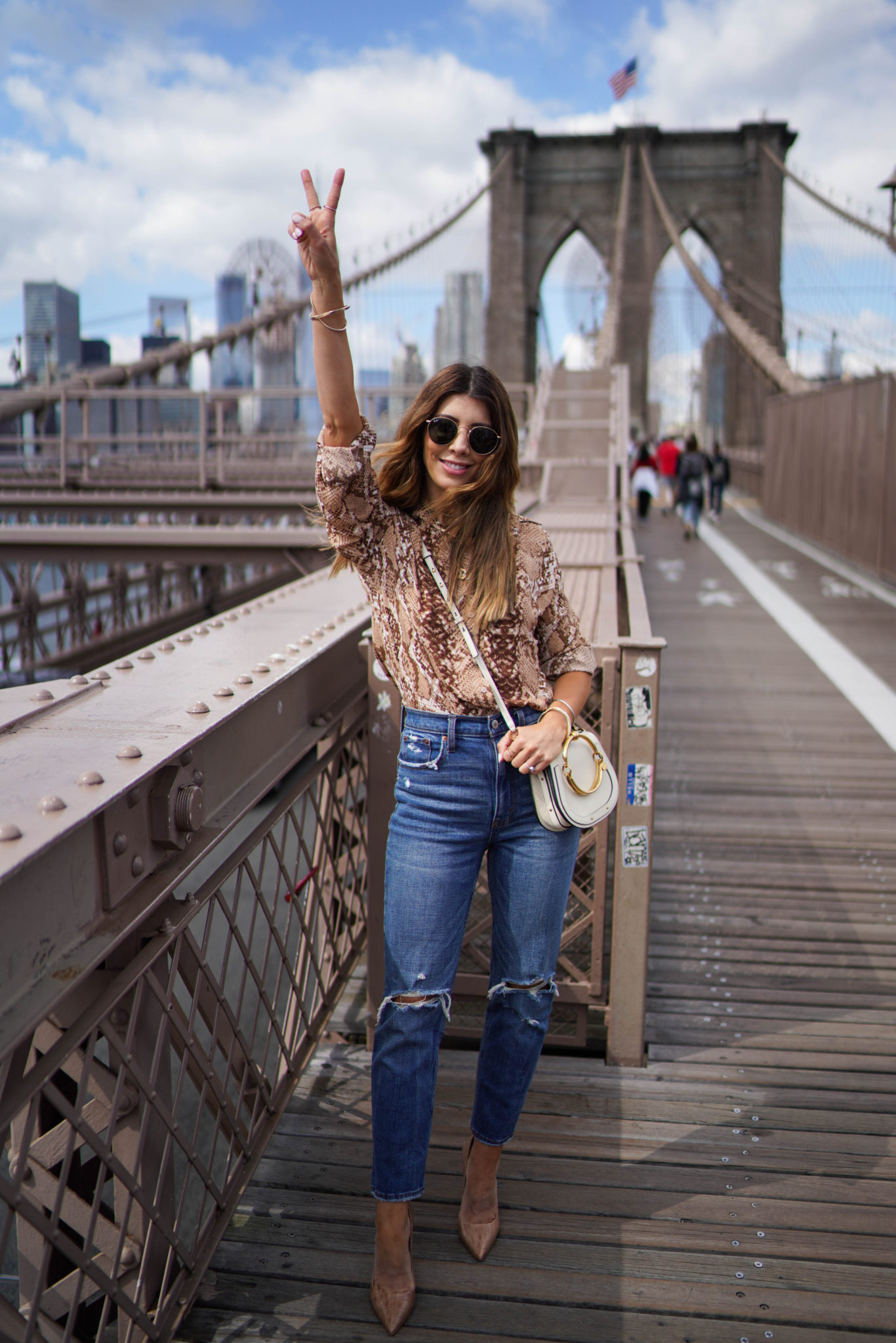 All Things Snakeskin Print by popular San Francisco fashion blog, The Girl in the Yellow Dress: image of a woman standing on the Brooklyn Bridge and wearing a H&M Long-sleeved Blouse, Abercrombie and Fitch Curve Love Ultra High Rise Ankle Straight Jeans, Nordstrom Steve Madden Prance Pump, Neiman Marcus Chloe Nile Small Bracelet Crossbody Bag, and Nordstrom Ray-Ban Icons 53mm Retro Sunglasses.