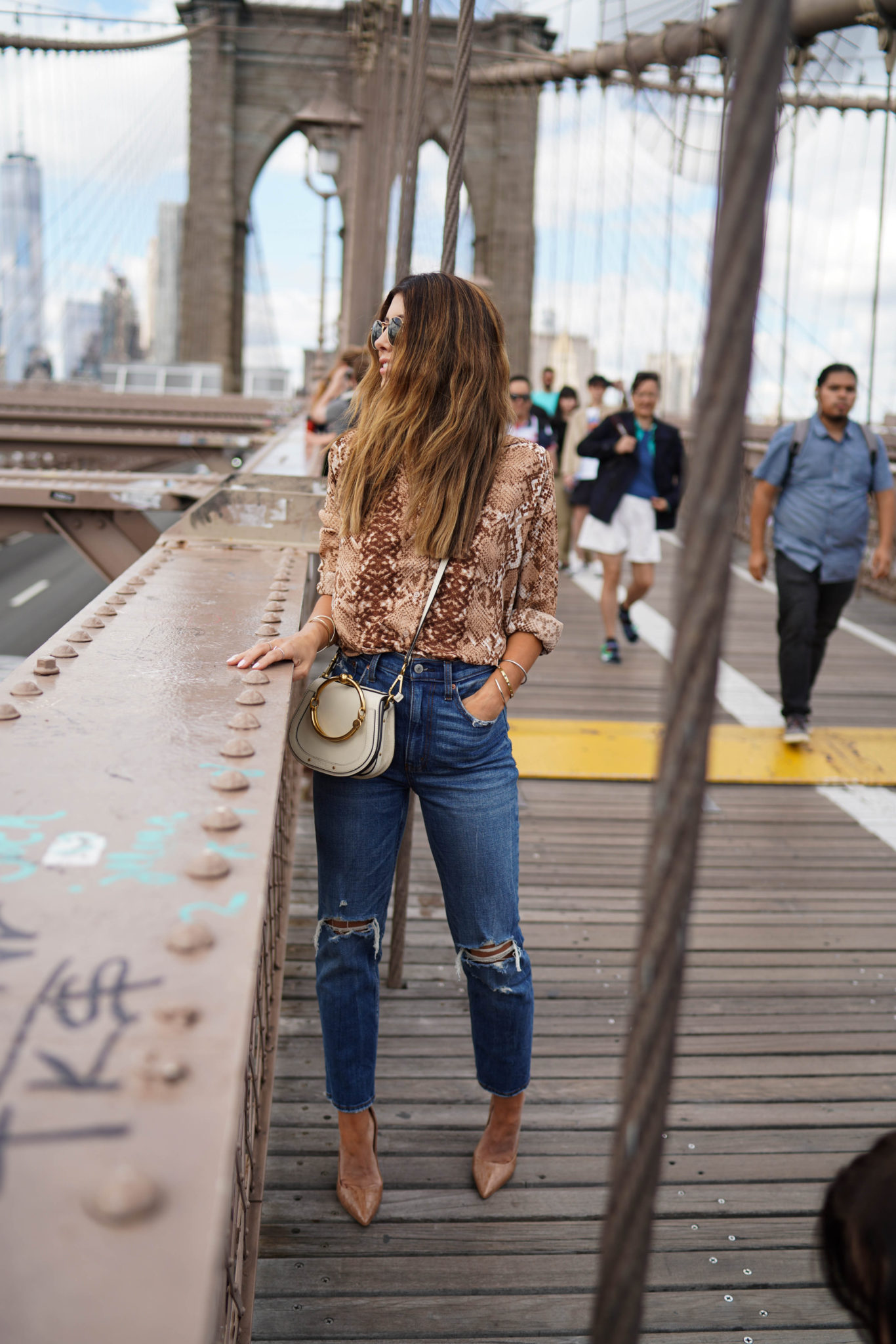 All Things Snakeskin Print by popular San Francisco fashion blog, The Girl in the Yellow Dress: image of a woman standing on the Brooklyn Bridge and wearing a H&M Long-sleeved Blouse, Abercrombie and Fitch Curve Love Ultra High Rise Ankle Straight Jeans, Nordstrom Steve Madden Prance Pump, Neiman Marcus Chloe Nile Small Bracelet Crossbody Bag, and Nordstrom Ray-Ban Icons 53mm Retro Sunglasses.