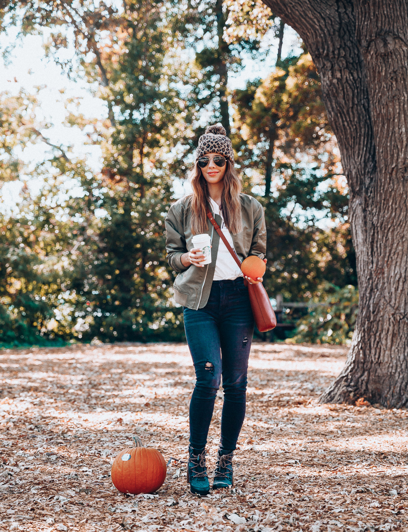 4 Fall Trends to Try by popular San Francisco fashion blog, The Girl in the Yellow Dress: image of a woman standing outside in a pile of leaves and wearing a Sole Society LEOPARD BEANIE W/ POM, EverEve Good American Bomber Jacket, Nordstrom Top Shop Jamie High Waist Ripped Hem Skinny Jeans, Evereve Sorel Blake Lace Up Bootie, Nordstrom Ray-Ban Standard Original 58mm Aviator Sunglasses, and Evereve Sol Angeles Grateful Tee.