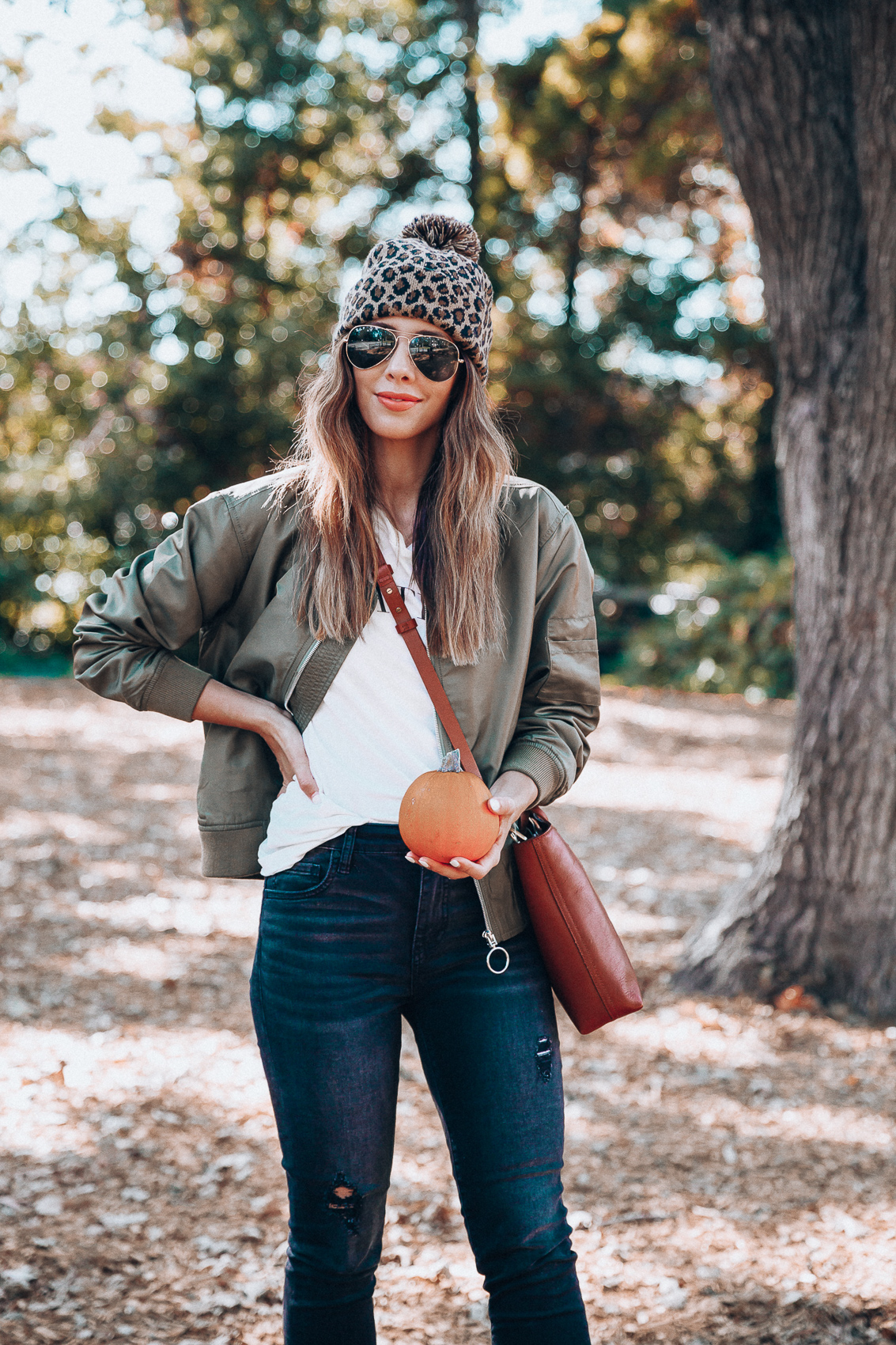 4 Fall Trends to Try by popular San Francisco fashion blog, The Girl in the Yellow Dress: image of a woman standing outside in a pile of leaves and wearing a Sole Society LEOPARD BEANIE W/ POM, EverEve Good American Bomber Jacket, Nordstrom Top Shop Jamie High Waist Ripped Hem Skinny Jeans, Evereve Sorel Blake Lace Up Bootie, Nordstrom Ray-Ban Standard Original 58mm Aviator Sunglasses, and Evereve Sol Angeles Grateful Tee.