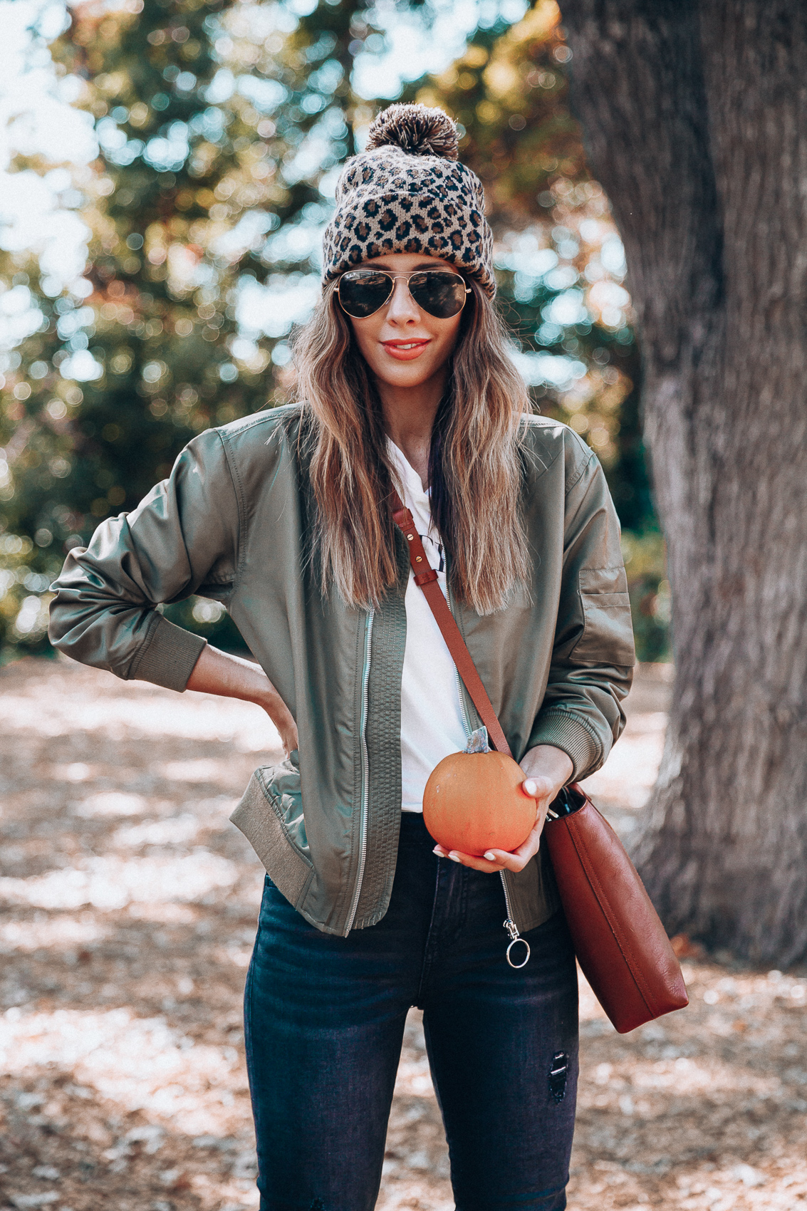 4 Fall Trends to Try by popular San Francisco fashion blog, The Girl in the Yellow Dress: image of a woman standing outside in a pile of leaves and wearing a Sole Society LEOPARD BEANIE W/ POM, EverEve Good American Bomber Jacket, Nordstrom Top Shop Jamie High Waist Ripped Hem Skinny Jeans, Evereve Sorel Blake Lace Up Bootie, Nordstrom Ray-Ban Standard Original 58mm Aviator Sunglasses, and Evereve Sol Angeles Grateful Tee.