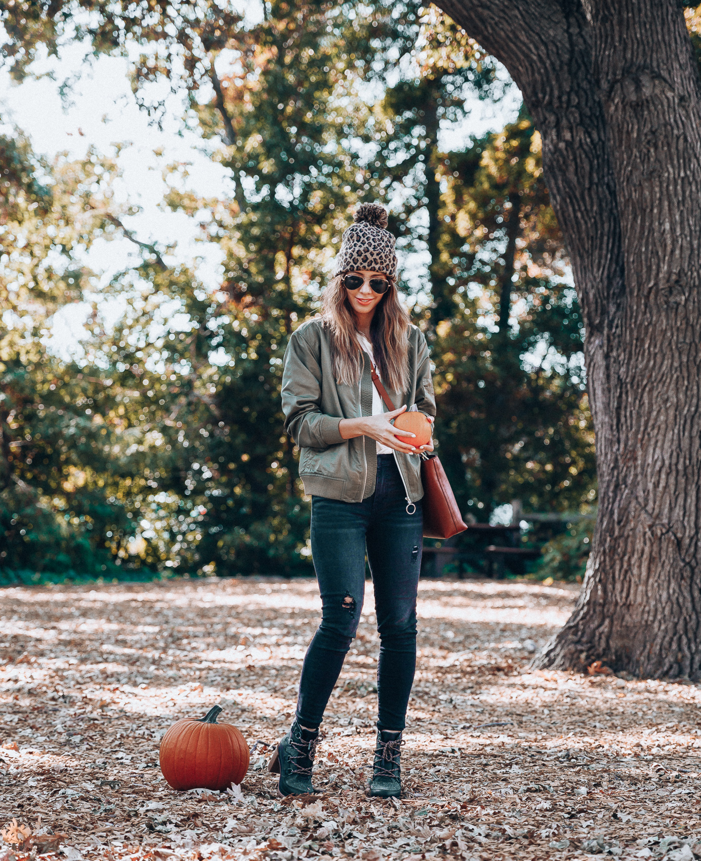 4 Fall Trends to Try by popular San Francisco fashion blog, The Girl in the Yellow Dress: image of a woman standing outside in a pile of leaves and wearing a Sole Society LEOPARD BEANIE W/ POM, EverEve Good American Bomber Jacket, Nordstrom Top Shop Jamie High Waist Ripped Hem Skinny Jeans, Evereve Sorel Blake Lace Up Bootie, Nordstrom Ray-Ban Standard Original 58mm Aviator Sunglasses, and Evereve Sol Angeles Grateful Tee.