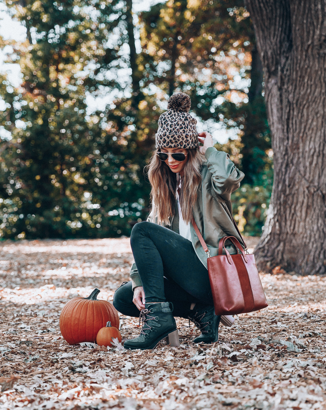 4 Fall Trends to Try by popular San Francisco fashion blog, The Girl in the Yellow Dress: image of a woman standing outside in a pile of leaves and wearing a Sole Society LEOPARD BEANIE W/ POM, EverEve Good American Bomber Jacket, Nordstrom Top Shop Jamie High Waist Ripped Hem Skinny Jeans, Evereve Sorel Blake Lace Up Bootie, Nordstrom Ray-Ban Standard Original 58mm Aviator Sunglasses, and Evereve Sol Angeles Grateful Tee.