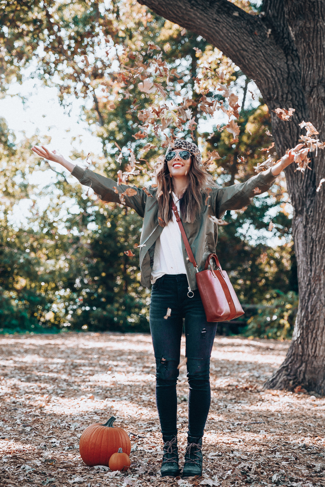 4 Fall Trends to Try by popular San Francisco fashion blog, The Girl in the Yellow Dress: image of a woman standing outside in a pile of leaves and wearing a Sole Society LEOPARD BEANIE W/ POM, EverEve Good American Bomber Jacket, Nordstrom Top Shop Jamie High Waist Ripped Hem Skinny Jeans, Evereve Sorel Blake Lace Up Bootie, Nordstrom Ray-Ban Standard Original 58mm Aviator Sunglasses, and Evereve Sol Angeles Grateful Tee.