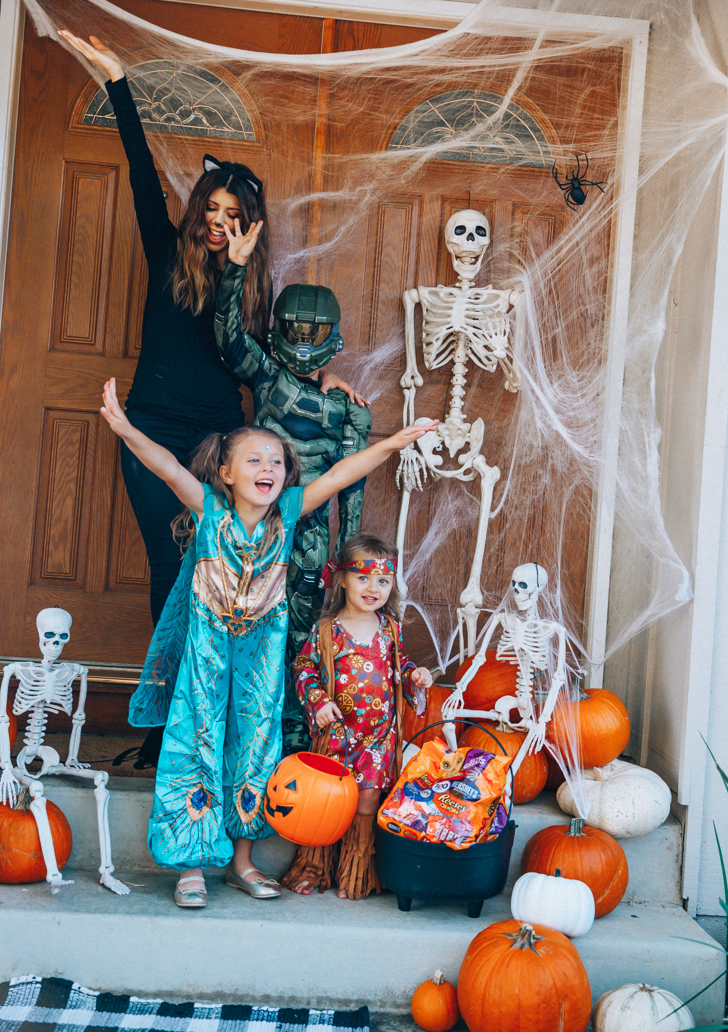 Spooky Halloween Front Porch Decor from Walmart by popular San Francisco life and style blog, The Girl in the Yellow Dress: image of a family standing on their front porch that's decorated with a Walmart 5ft Full Body Skeleton Props with Movable Joints for Halloween Party Decoration, Halloween Dutch Kettle Cauldron 14 Inch Black Plastic Party Accessory (1/Pkg) Pkg/1  Report incorrect product info or prohibited items Halloween Dutch Kettle Cauldron 14 Inch Black Plastic Party Accessory, Walmart Poseable Skeleton 20in Halloween Decoration, Pumpkins, and Walmart Stretchable Spider Web and Spider Halloween Decoration and wearing a Walmart Girl's Jasmine Teal Classic Halloween Costume, Walmart 60's Hippie with Fringe Child Halloween Costume, Walmart Halo Boys' Master Chief Classic Muscle Costume, Walmart Sequin cat ears, Walmart Jordache  Women's Super Soft Mid Rise Skinny Jean, Walmart Seven Dials  Womens Seven Dials Teatime Sock Booties, and Walmart TheLovely  Women's Long Sleeve Crew Neck Basic T-Shirt Top.