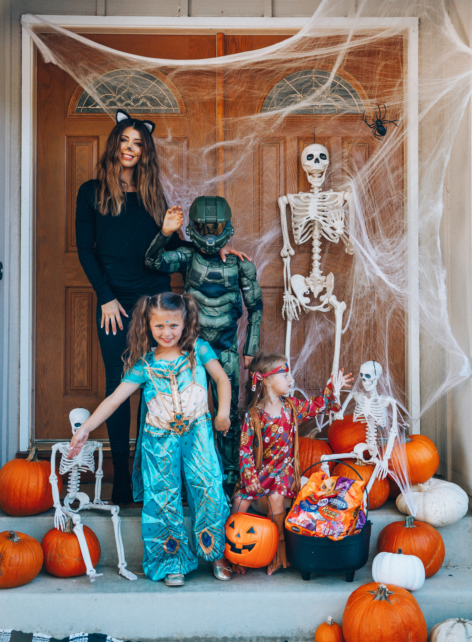 Spooky Halloween Front Porch Decor from Walmart by popular San Francisco life and style blog, The Girl in the Yellow Dress: image of a family standing on their front porch that's decorated with a Walmart 5ft Full Body Skeleton Props with Movable Joints for Halloween Party Decoration, Halloween Dutch Kettle Cauldron 14 Inch Black Plastic Party Accessory (1/Pkg) Pkg/1  Report incorrect product info or prohibited items Halloween Dutch Kettle Cauldron 14 Inch Black Plastic Party Accessory, Walmart Poseable Skeleton 20in Halloween Decoration, Pumpkins, and Walmart Stretchable Spider Web and Spider Halloween Decoration and wearing a Walmart Girl's Jasmine Teal Classic Halloween Costume, Walmart 60's Hippie with Fringe Child Halloween Costume, Walmart Halo Boys' Master Chief Classic Muscle Costume, Walmart Sequin cat ears, Walmart Jordache  Women's Super Soft Mid Rise Skinny Jean, Walmart Seven Dials  Womens Seven Dials Teatime Sock Booties, and Walmart TheLovely  Women's Long Sleeve Crew Neck Basic T-Shirt Top.