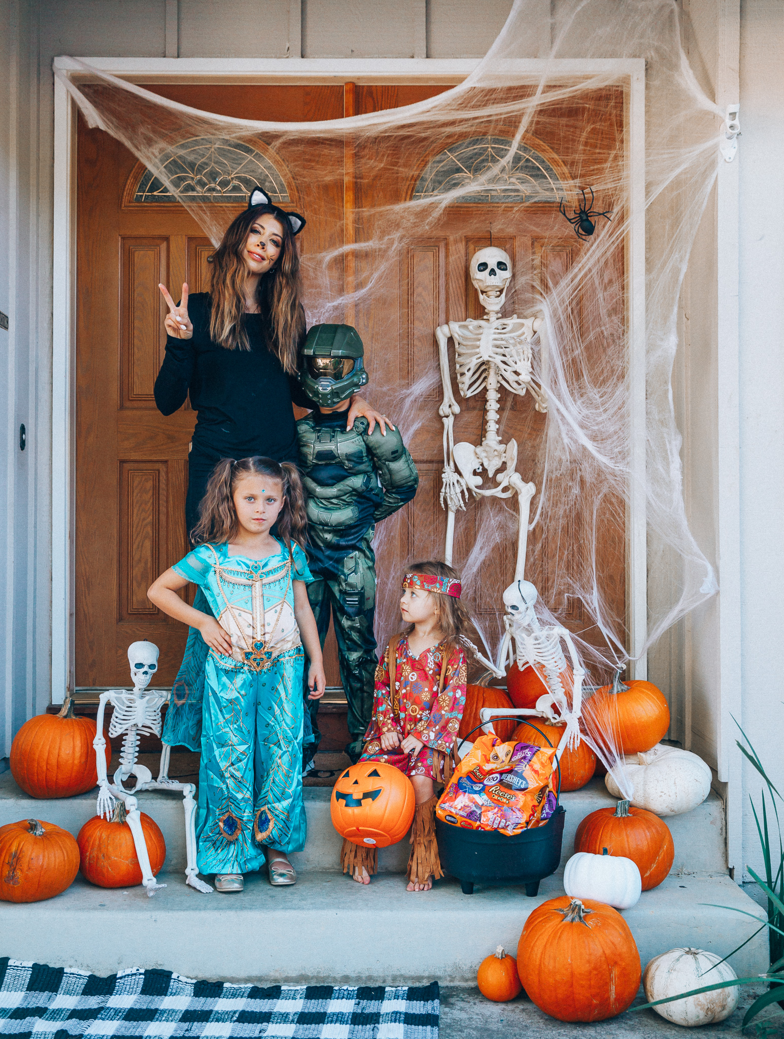 Spooky Halloween Front Porch Decor from Walmart by popular San Francisco life and style blog, The Girl in the Yellow Dress: image of a family standing on their front porch that's decorated with a Walmart 5ft Full Body Skeleton Props with Movable Joints for Halloween Party Decoration, Halloween Dutch Kettle Cauldron 14 Inch Black Plastic Party Accessory (1/Pkg) Pkg/1  Report incorrect product info or prohibited items Halloween Dutch Kettle Cauldron 14 Inch Black Plastic Party Accessory, Walmart Poseable Skeleton 20in Halloween Decoration, Pumpkins, and Walmart Stretchable Spider Web and Spider Halloween Decoration and wearing a Walmart Girl's Jasmine Teal Classic Halloween Costume, Walmart 60's Hippie with Fringe Child Halloween Costume, Walmart Halo Boys' Master Chief Classic Muscle Costume, Walmart Sequin cat ears, Walmart Jordache  Women's Super Soft Mid Rise Skinny Jean, Walmart Seven Dials  Womens Seven Dials Teatime Sock Booties, and Walmart TheLovely  Women's Long Sleeve Crew Neck Basic T-Shirt Top.