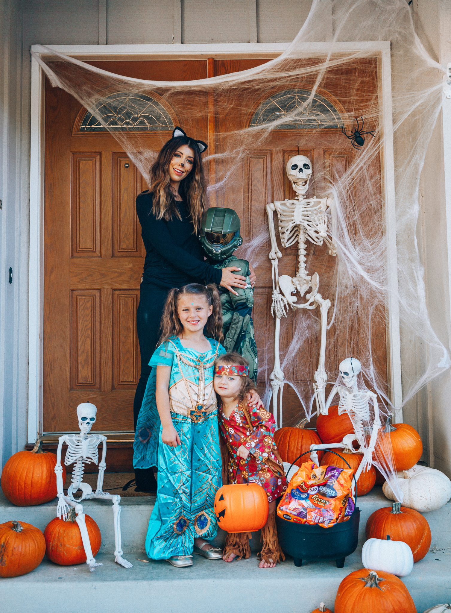 Spooky Halloween Front Porch Decor from Walmart by popular San Francisco life and style blog, The Girl in the Yellow Dress: image of a family standing on their front porch that's decorated with a Walmart 5ft Full Body Skeleton Props with Movable Joints for Halloween Party Decoration, Halloween Dutch Kettle Cauldron 14 Inch Black Plastic Party Accessory (1/Pkg) Pkg/1  Report incorrect product info or prohibited items Halloween Dutch Kettle Cauldron 14 Inch Black Plastic Party Accessory, Walmart Poseable Skeleton 20in Halloween Decoration, Pumpkins, and Walmart Stretchable Spider Web and Spider Halloween Decoration and wearing a Walmart Girl's Jasmine Teal Classic Halloween Costume, Walmart 60's Hippie with Fringe Child Halloween Costume, Walmart Halo Boys' Master Chief Classic Muscle Costume, Walmart Sequin cat ears, Walmart Jordache  Women's Super Soft Mid Rise Skinny Jean, Walmart Seven Dials  Womens Seven Dials Teatime Sock Booties, and Walmart TheLovely  Women's Long Sleeve Crew Neck Basic T-Shirt Top.