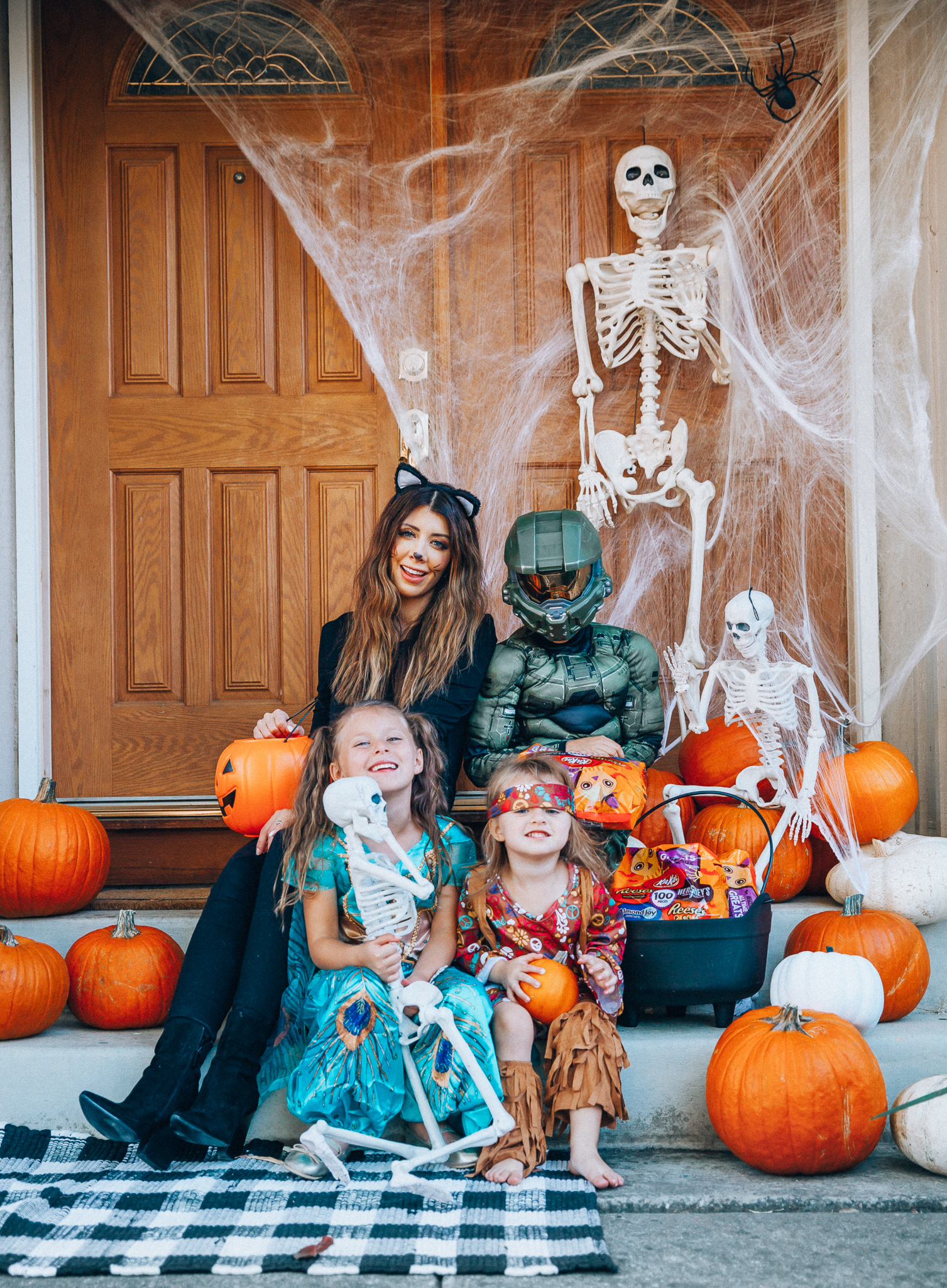 Spooky Halloween Front Porch Decor from Walmart by popular San Francisco life and style blog, The Girl in the Yellow Dress: image of a family standing on their front porch that's decorated with a Walmart 5ft Full Body Skeleton Props with Movable Joints for Halloween Party Decoration, Halloween Dutch Kettle Cauldron 14 Inch Black Plastic Party Accessory (1/Pkg) Pkg/1  Report incorrect product info or prohibited items Halloween Dutch Kettle Cauldron 14 Inch Black Plastic Party Accessory, Walmart Poseable Skeleton 20in Halloween Decoration, Pumpkins, and Walmart Stretchable Spider Web and Spider Halloween Decoration and wearing a Walmart Girl's Jasmine Teal Classic Halloween Costume, Walmart 60's Hippie with Fringe Child Halloween Costume, Walmart Halo Boys' Master Chief Classic Muscle Costume, Walmart Sequin cat ears, Walmart Jordache  Women's Super Soft Mid Rise Skinny Jean, Walmart Seven Dials  Womens Seven Dials Teatime Sock Booties, and Walmart TheLovely  Women's Long Sleeve Crew Neck Basic T-Shirt Top.