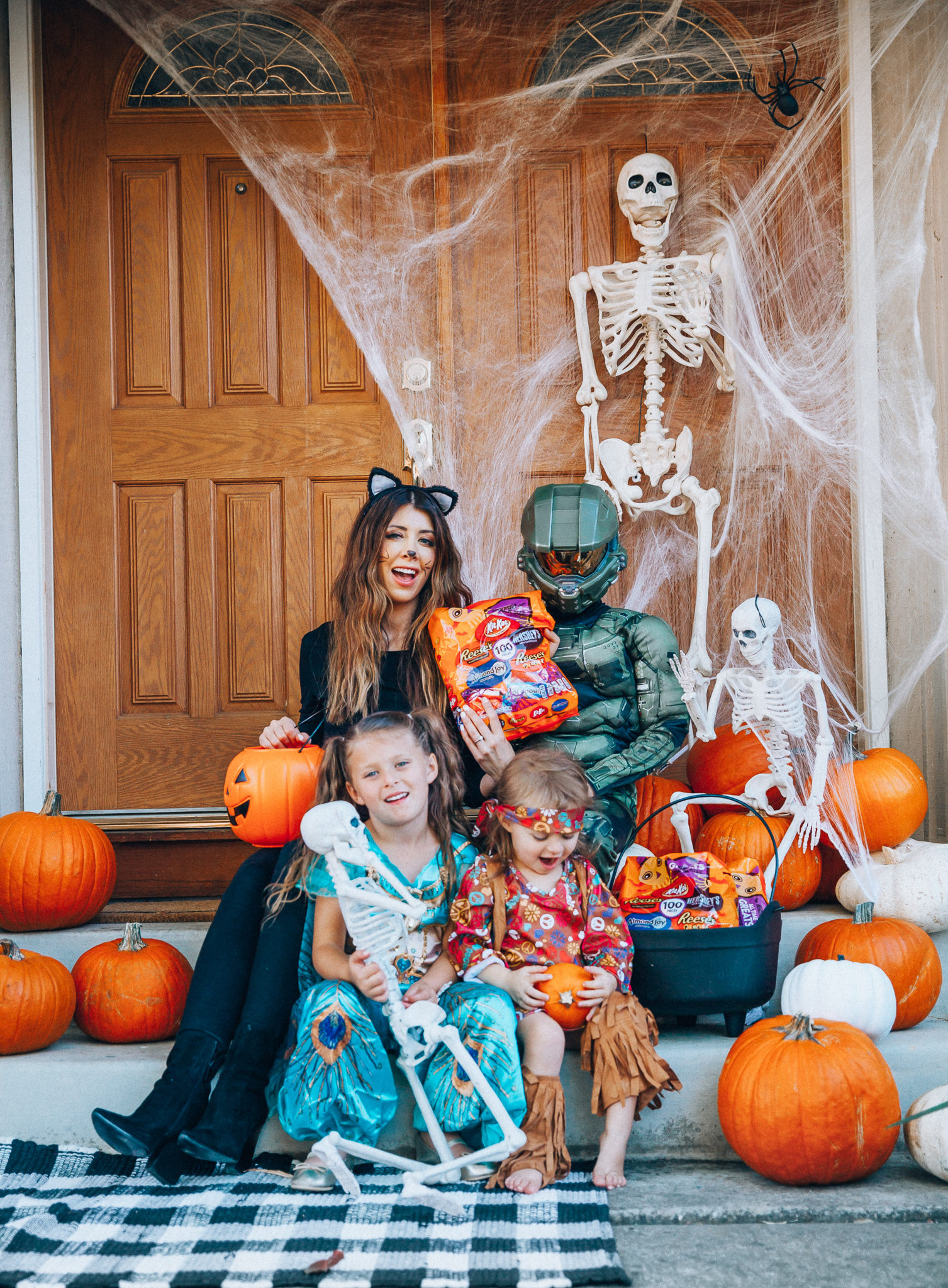 Spooky Halloween Front Porch Decor from Walmart by popular San Francisco life and style blog, The Girl in the Yellow Dress: image of a family standing on their front porch that's decorated with a Walmart 5ft Full Body Skeleton Props with Movable Joints for Halloween Party Decoration, Halloween Dutch Kettle Cauldron 14 Inch Black Plastic Party Accessory (1/Pkg) Pkg/1  Report incorrect product info or prohibited items Halloween Dutch Kettle Cauldron 14 Inch Black Plastic Party Accessory, Walmart Poseable Skeleton 20in Halloween Decoration, Pumpkins, and Walmart Stretchable Spider Web and Spider Halloween Decoration and wearing a Walmart Girl's Jasmine Teal Classic Halloween Costume, Walmart 60's Hippie with Fringe Child Halloween Costume, Walmart Halo Boys' Master Chief Classic Muscle Costume, Walmart Sequin cat ears, Walmart Jordache  Women's Super Soft Mid Rise Skinny Jean, Walmart Seven Dials  Womens Seven Dials Teatime Sock Booties, and Walmart TheLovely  Women's Long Sleeve Crew Neck Basic T-Shirt Top.