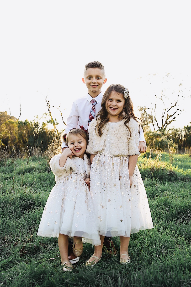 Merry Christmas Wishes 2019 by popular San Francisco life and style blog, The Girl in the Yellow Dress: image of a brother and two sisters standing together outside in a grassy field and wearing H&M Sequined Tulle Dress, and Amazon THEE BRON Girl's Toddler/Little Kid Ballet Mary Jane Flat Shoes.