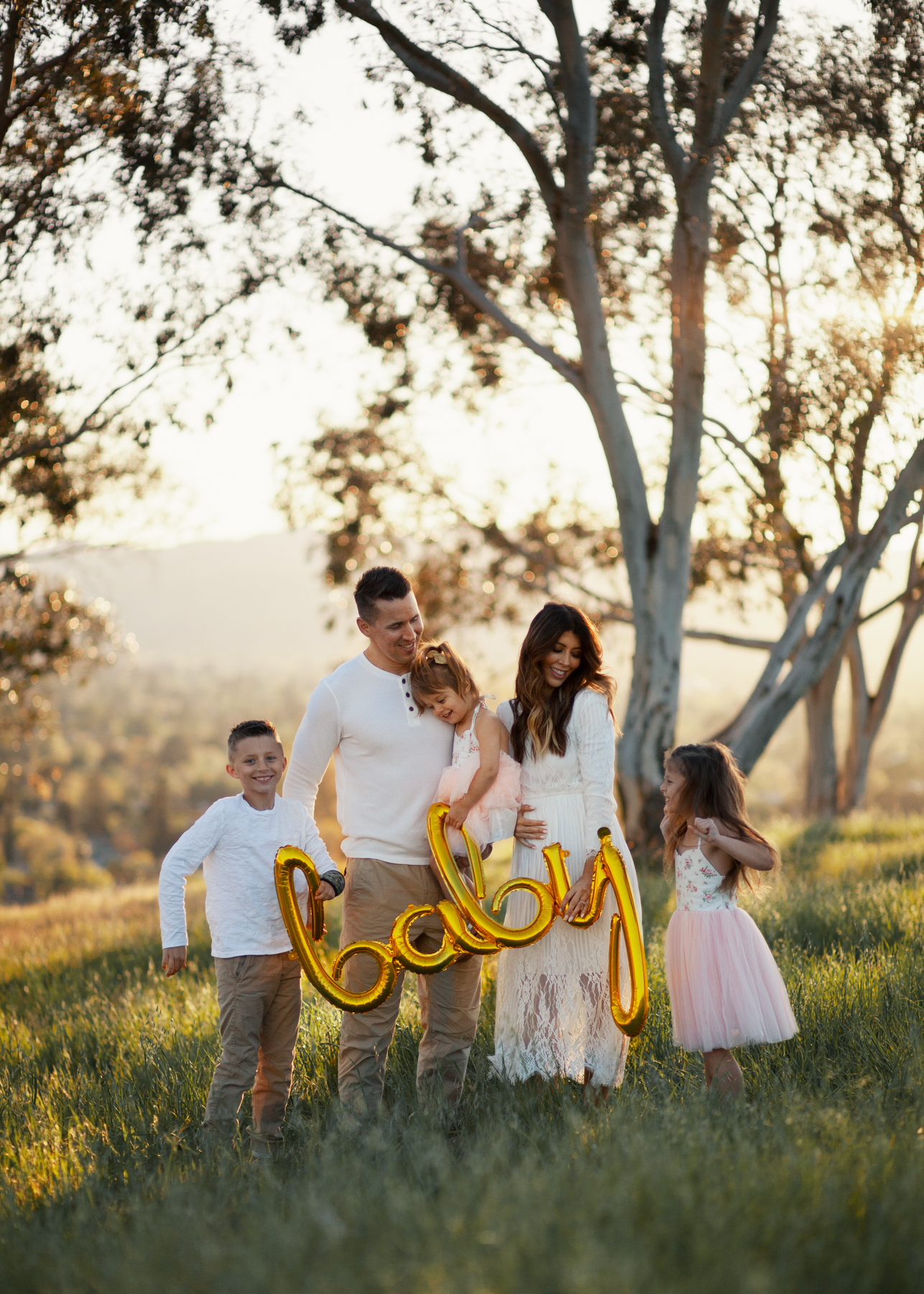 Family Pregnancy Announcement by popular San Francisco lifestyle blog, The Girl in the Yellow Dress: image of a family standing in a field, holding a gold baby balloon and wearing a Nordstrom Yaro Ankle Strap Sandal SAM EDELMAN, Old Navy Soft-Washed Long-Sleeve Henley for Men, Aerie AE NE(X)T LEVEL KHAKI JOGGER, Nordstrom GrandPro Low Top Sneaker COLE HAAN, Amazon Flofallzique Baby Girls Dress Toddler Tutu Infant Floral Sundress Tulle Wedding Dress, Freshly Picked White Patent Malibu, Old Navy Softest Crew-Neck Long-Sleeve Tee for Boys, and Old Navy Built-In Flex Twill Joggers for Boys.