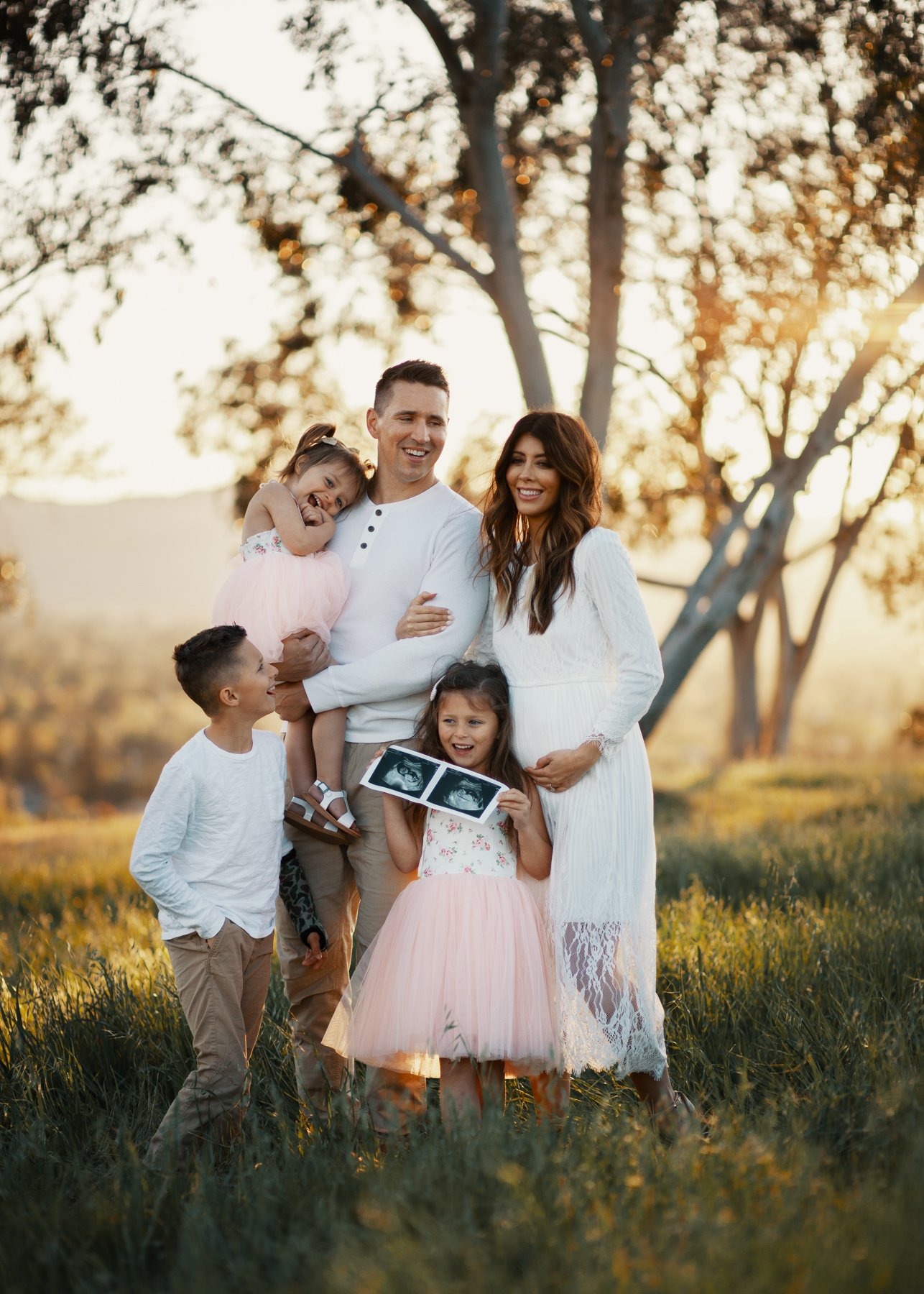 Family Pregnancy Announcement by popular San Francisco lifestyle blog, The Girl in the Yellow Dress: image of a family standing in a field, holding ultra sound photos and wearing a Nordstrom Yaro Ankle Strap Sandal SAM EDELMAN, Old Navy Soft-Washed Long-Sleeve Henley for Men, Aerie AE NE(X)T LEVEL KHAKI JOGGER, Nordstrom GrandPro Low Top Sneaker COLE HAAN, Amazon Flofallzique Baby Girls Dress Toddler Tutu Infant Floral Sundress Tulle Wedding Dress, Freshly Picked White Patent Malibu, Old Navy Softest Crew-Neck Long-Sleeve Tee for Boys, and Old Navy Built-In Flex Twill Joggers for Boys.