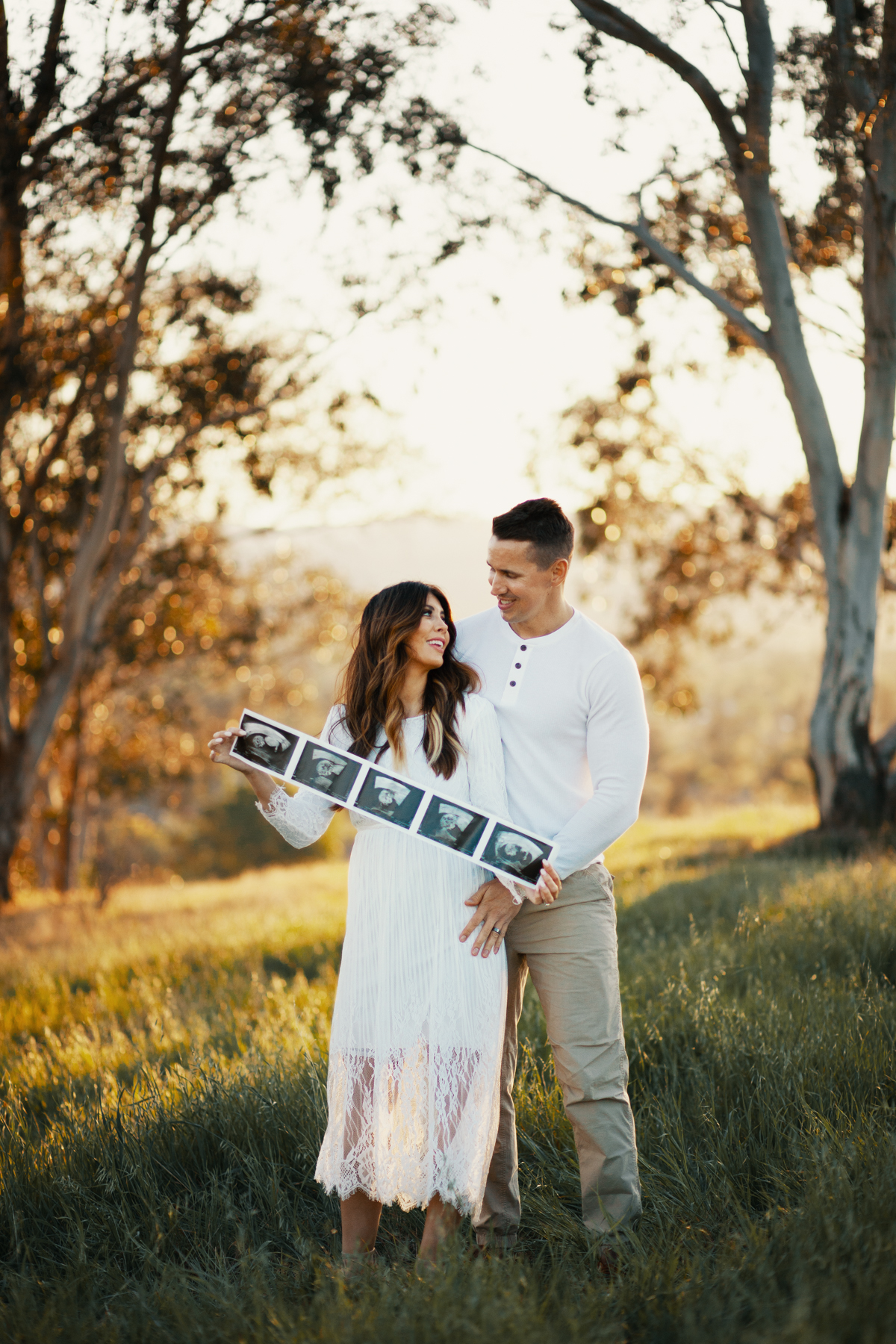 Family Pregnancy Announcement by popular San Francisco lifestyle blog, The Girl in the Yellow Dress: image of a husband and wife standing together in a field, holding some ultra sound pictures and wearing a Nordstrom Yaro Ankle Strap Sandal SAM EDELMAN, Old Navy Soft-Washed Long-Sleeve Henley for Men, Aerie AE NE(X)T LEVEL KHAKI JOGGER, and Nordstrom GrandPro Low Top Sneaker COLE HAAN.