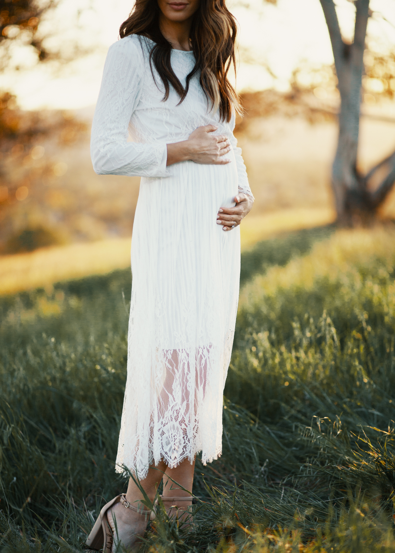 Family Pregnancy Announcement by popular San Francisco lifestyle blog, The Girl in the Yellow Dress: image of a pregnant woman holding her belly and standing in a field and wearing a Nordstrom Yaro Ankle Strap Sandal SAM EDELMAN and wearing a white lace dress.