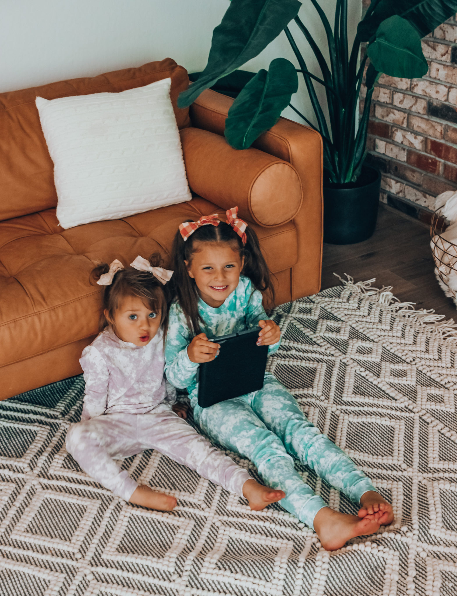 Messenger Kids Review by popular San Francisco lifestyle blog,The Girl in the Yellow Dress: image of two young girls wearing tie dye pajamas while sitting on the floor and holding a tablet. 